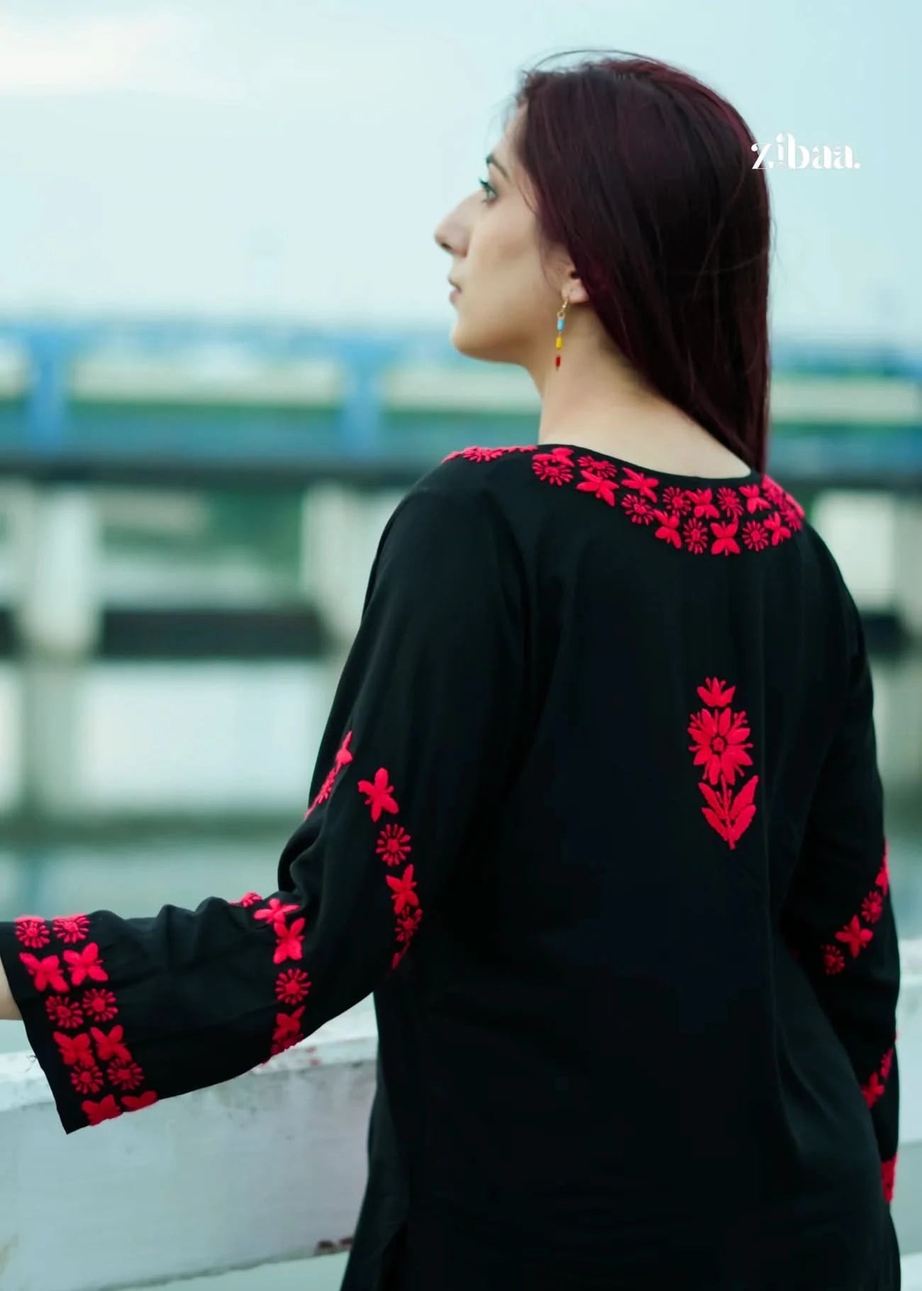 Woman wearing a black outfit with red floral embroidery against a blurred outdoor background