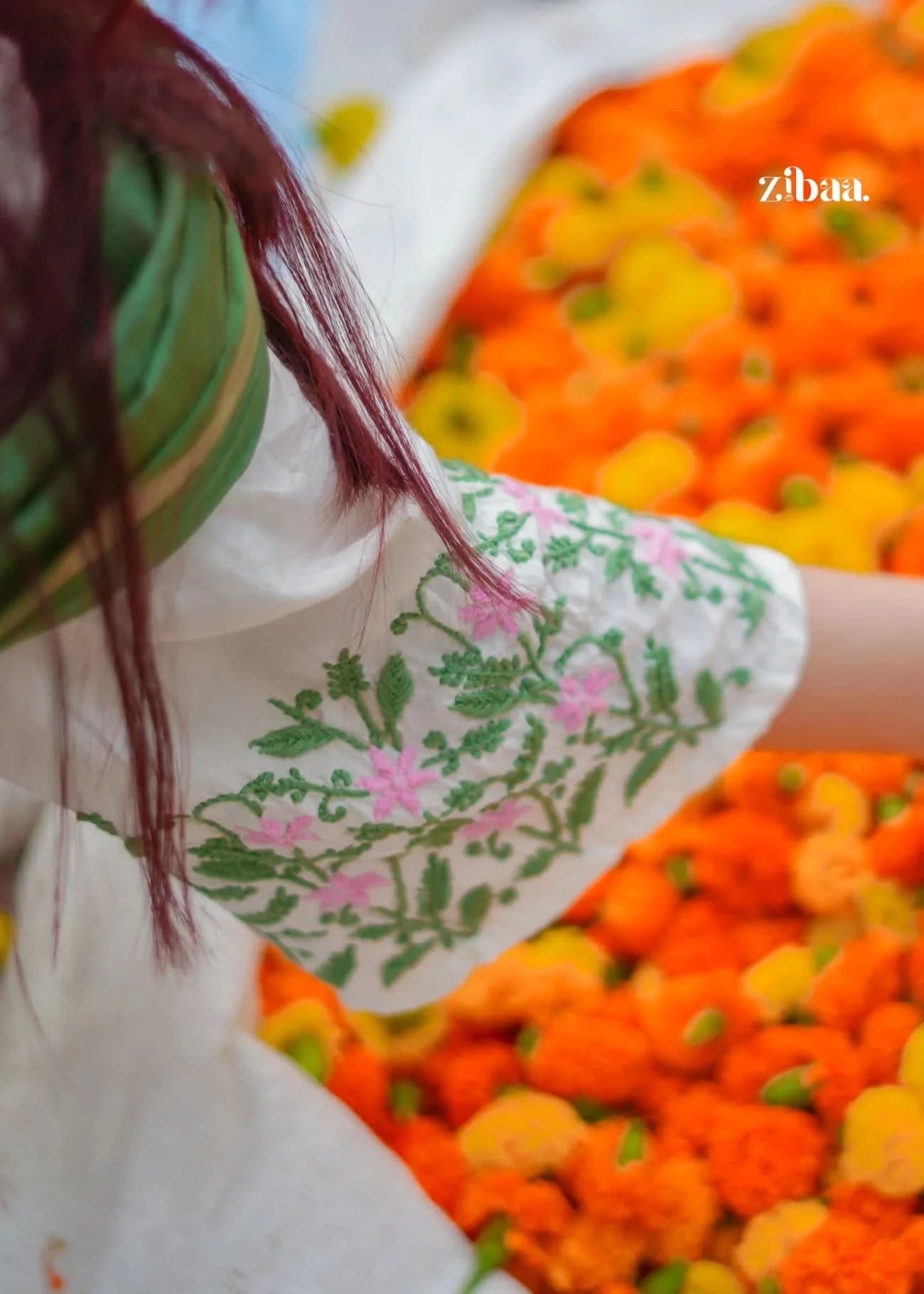 Person wearing a floral dress with a blurred background of orange and yellow flowers.