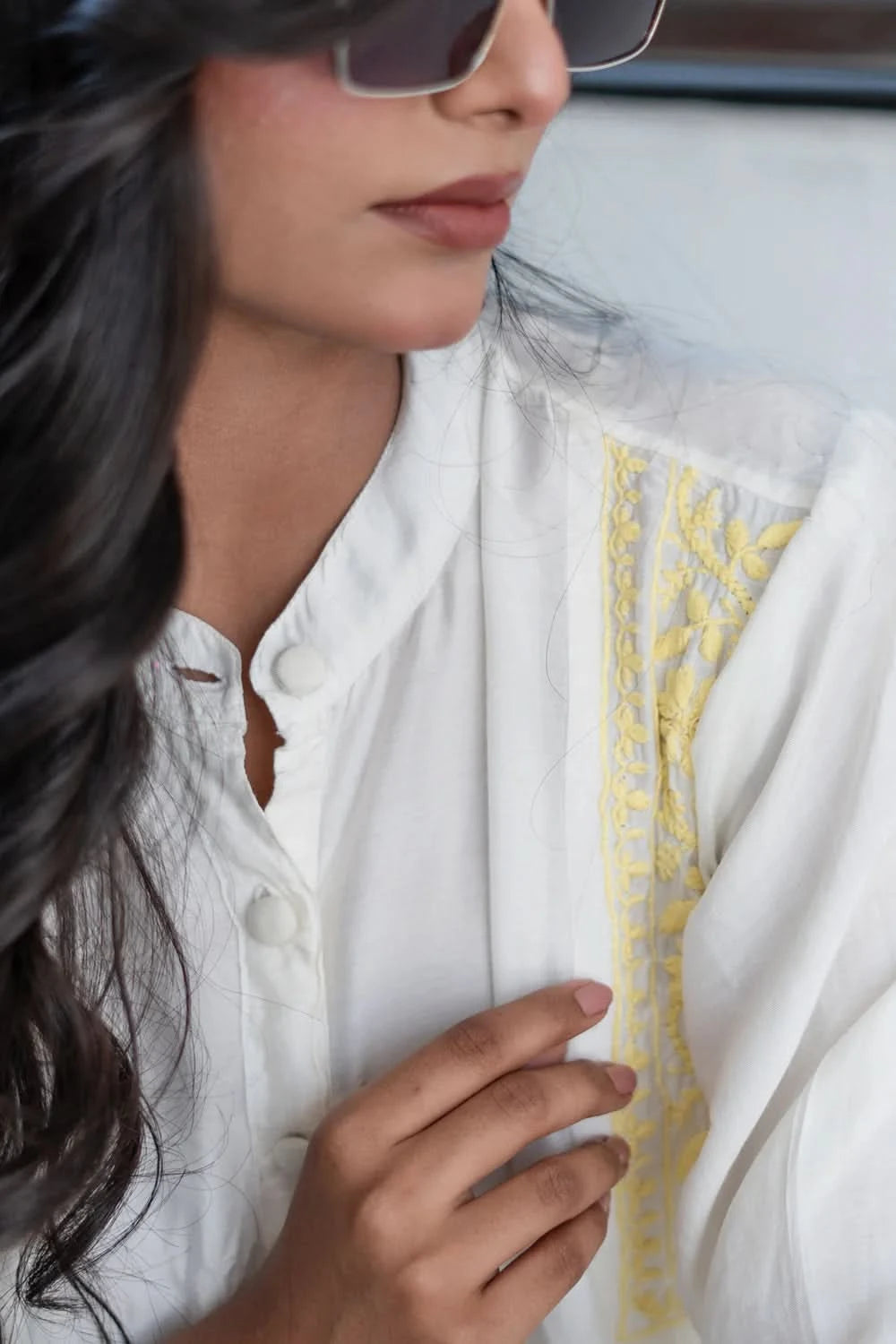 Woman wearing sunglasses and a white outfit with yellow patterns.