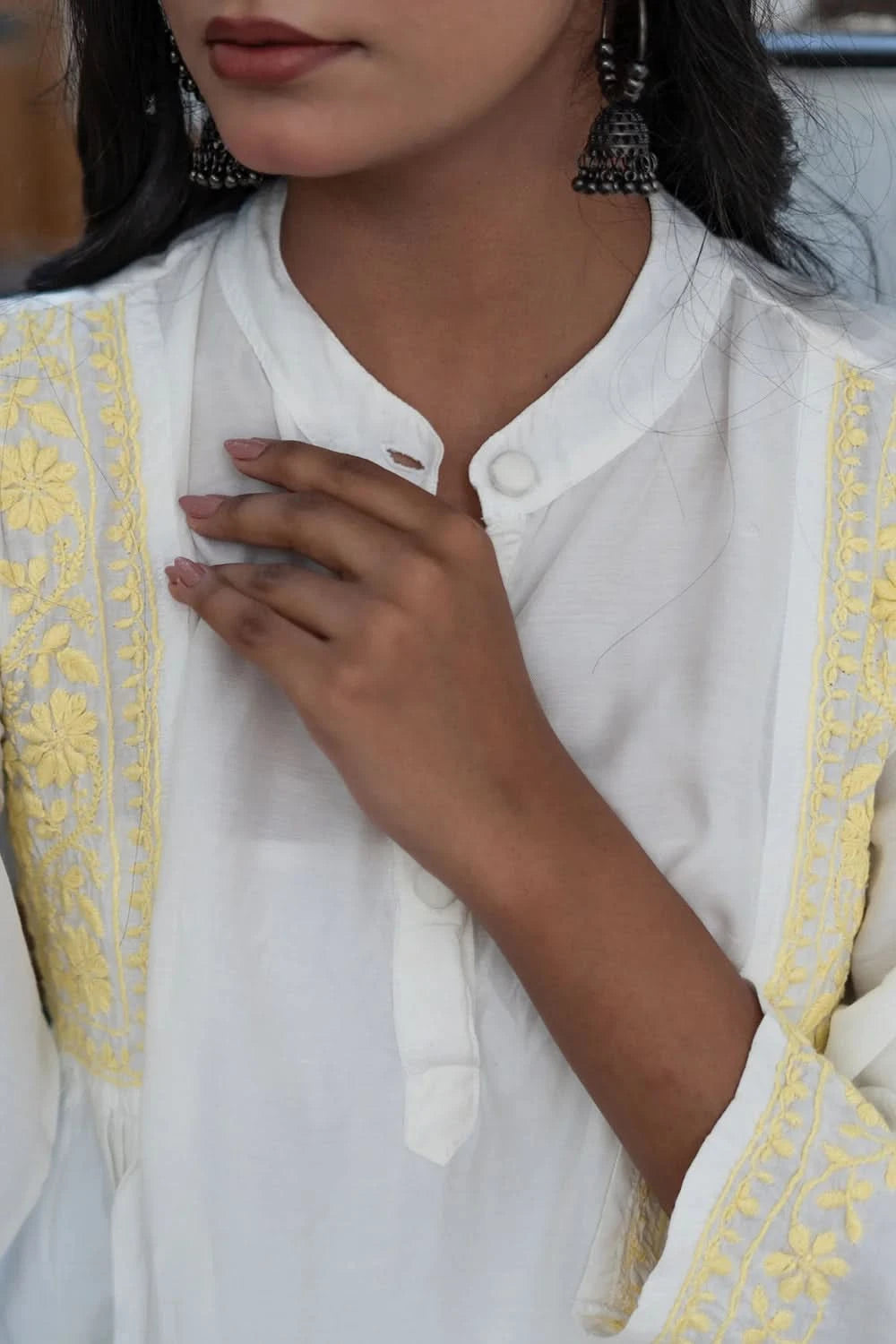 White outfit with yellow embroidery and a hand touching the chest.