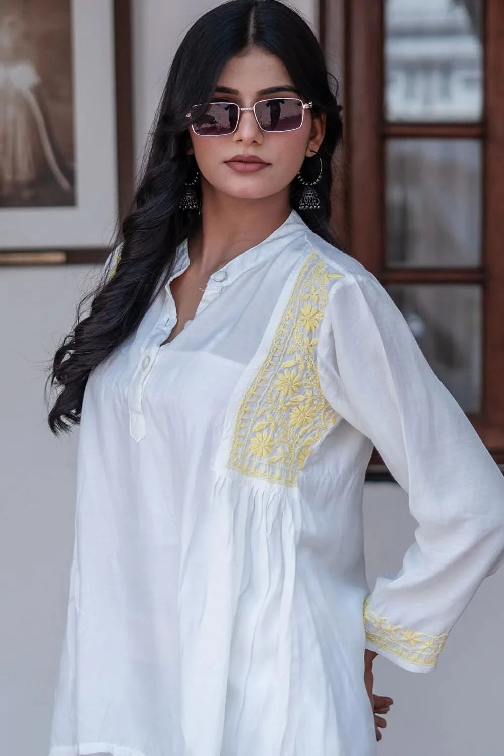 Woman wearing a white embroidered top with yellow details indoors.