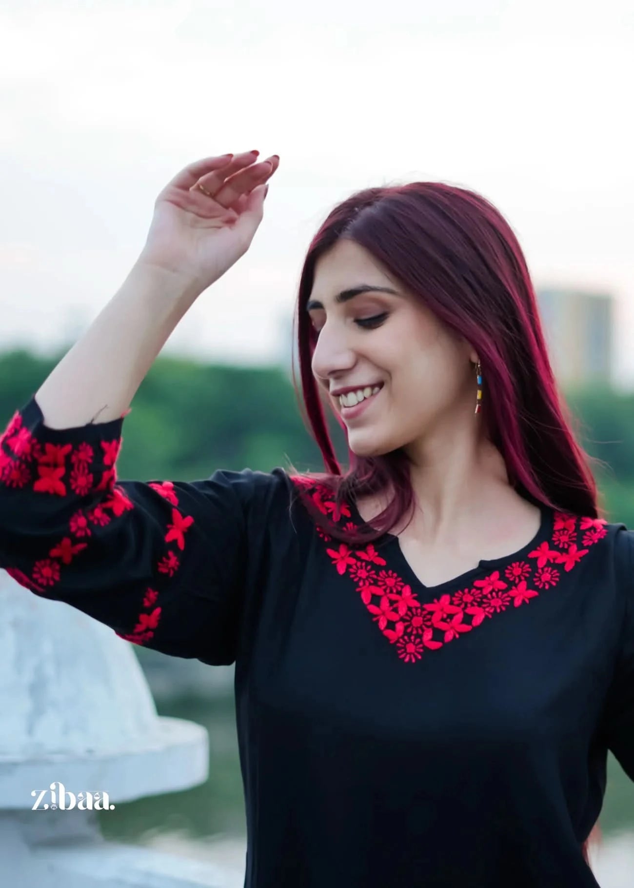 Woman wearing a black top with red embroidery, standing outdoors.