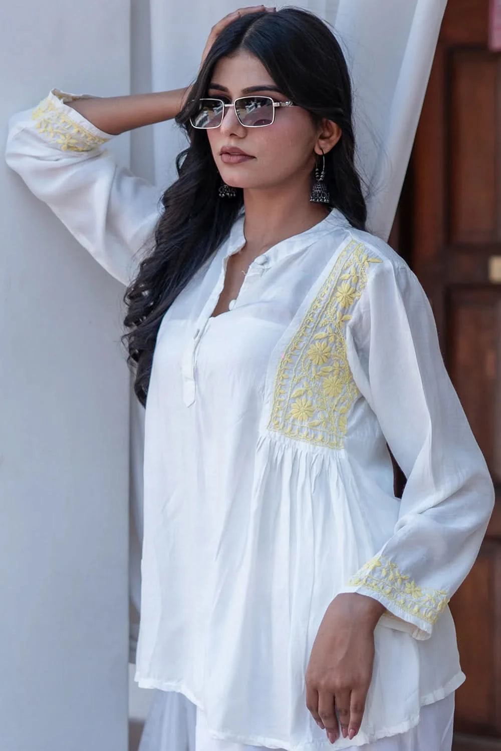Woman wearing a white embroidered top with yellow details against a neutral background