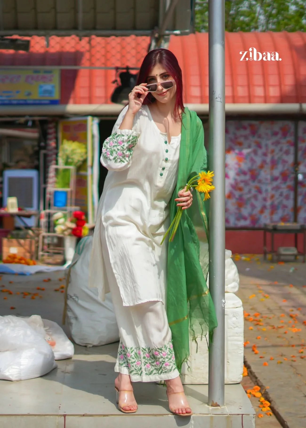 Woman in a white outfit with green dupatta holding flowers, standing outdoors.