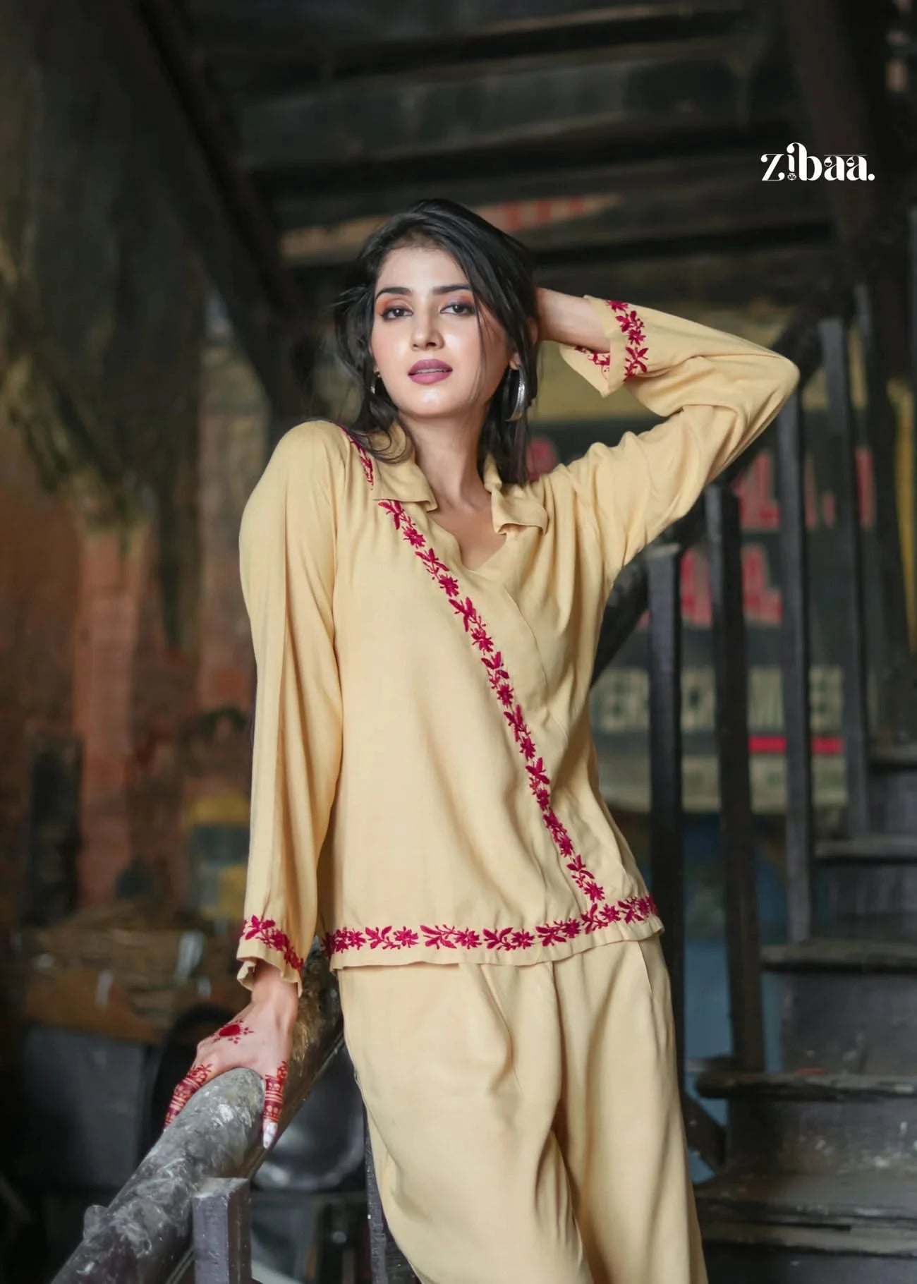stylish beige ethnic co-ord set outfit adorned with red floral embroidery. The model poses confidently on a rustic staircase, blending elegance with a bold city vibe. Ideal for festive and semi-formal occasions.