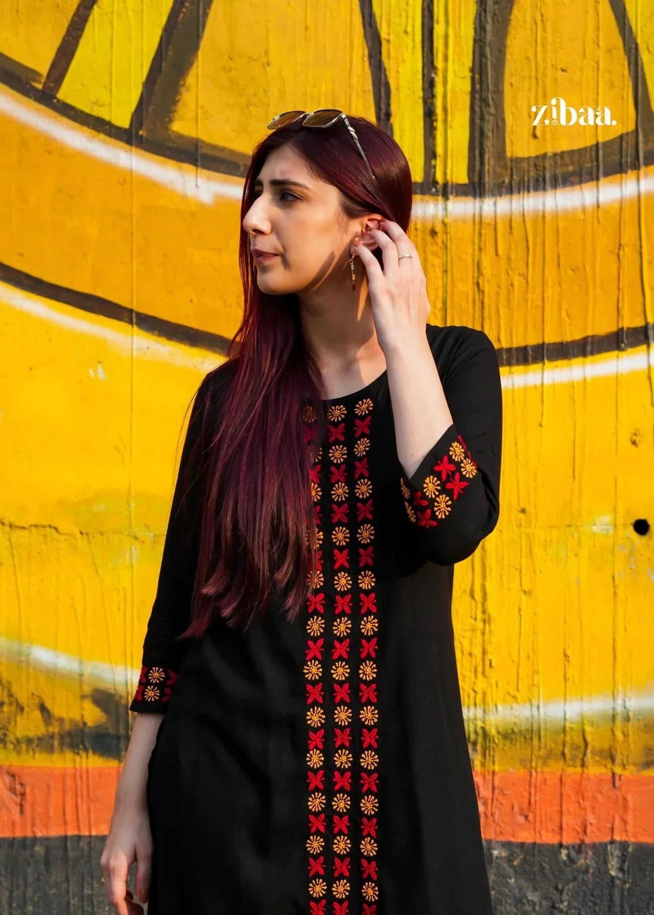Woman wearing a black chikankari kurta set with colorful embroidery against a vibrant yellow wall.