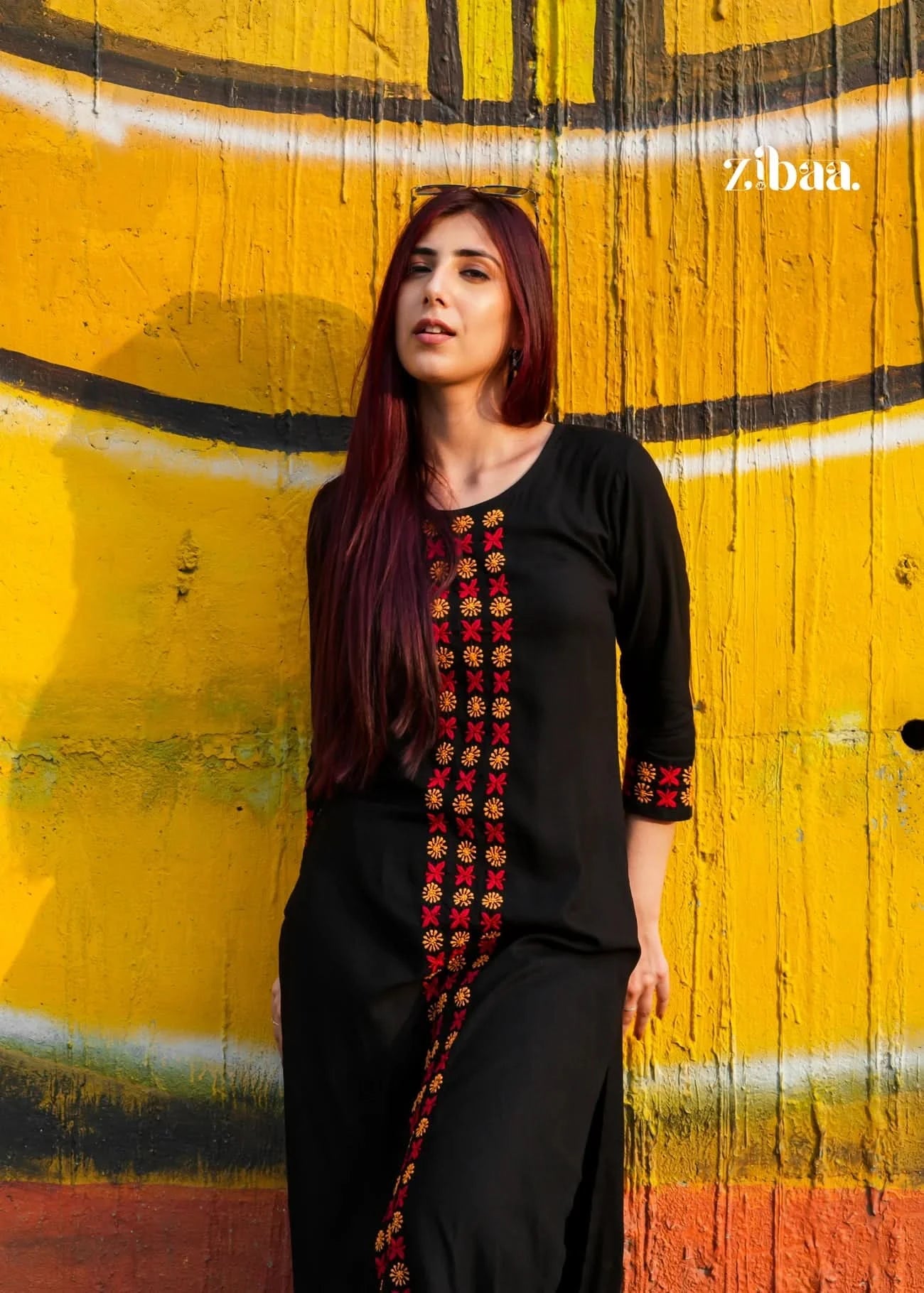 Woman in a black chikankari kurti set with colorful patterns standing against a yellow wall with graffiti.