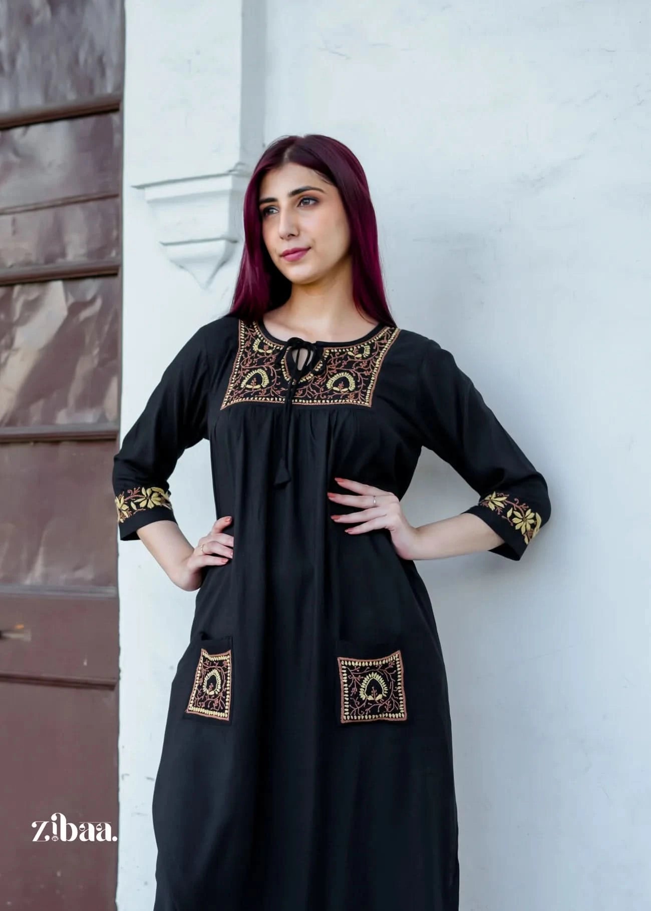 The model strikes a pose wearing a black chikankari kurti adorned with elegant golden embroidery on the pockets, cuffs, and neckline.