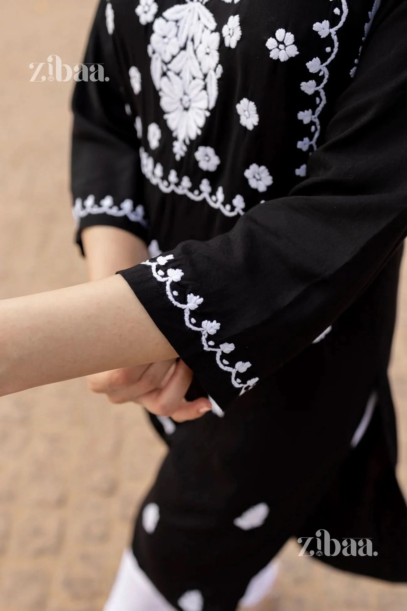 Close-up of a black Chikankari kurti showcasing delicate white embroidery on the sleeve and intricate floral patterns on the fabric.