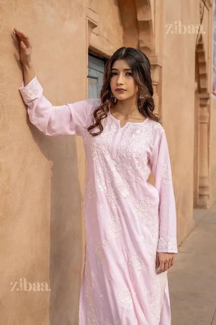 Model in a Pink Chikankari Kurti with white embroidery, posing stylishly against a rustic wooden door in a traditional outdoor setting