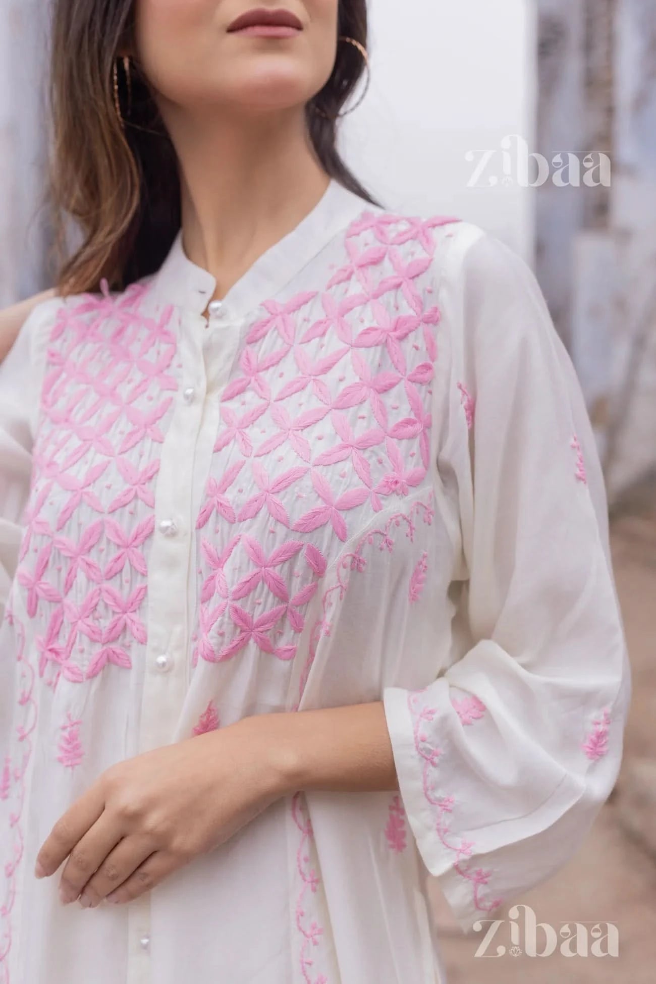 Contemporary style featuring a white chikankari kurta with hand-embroidered pink geometric designs, captured outside.