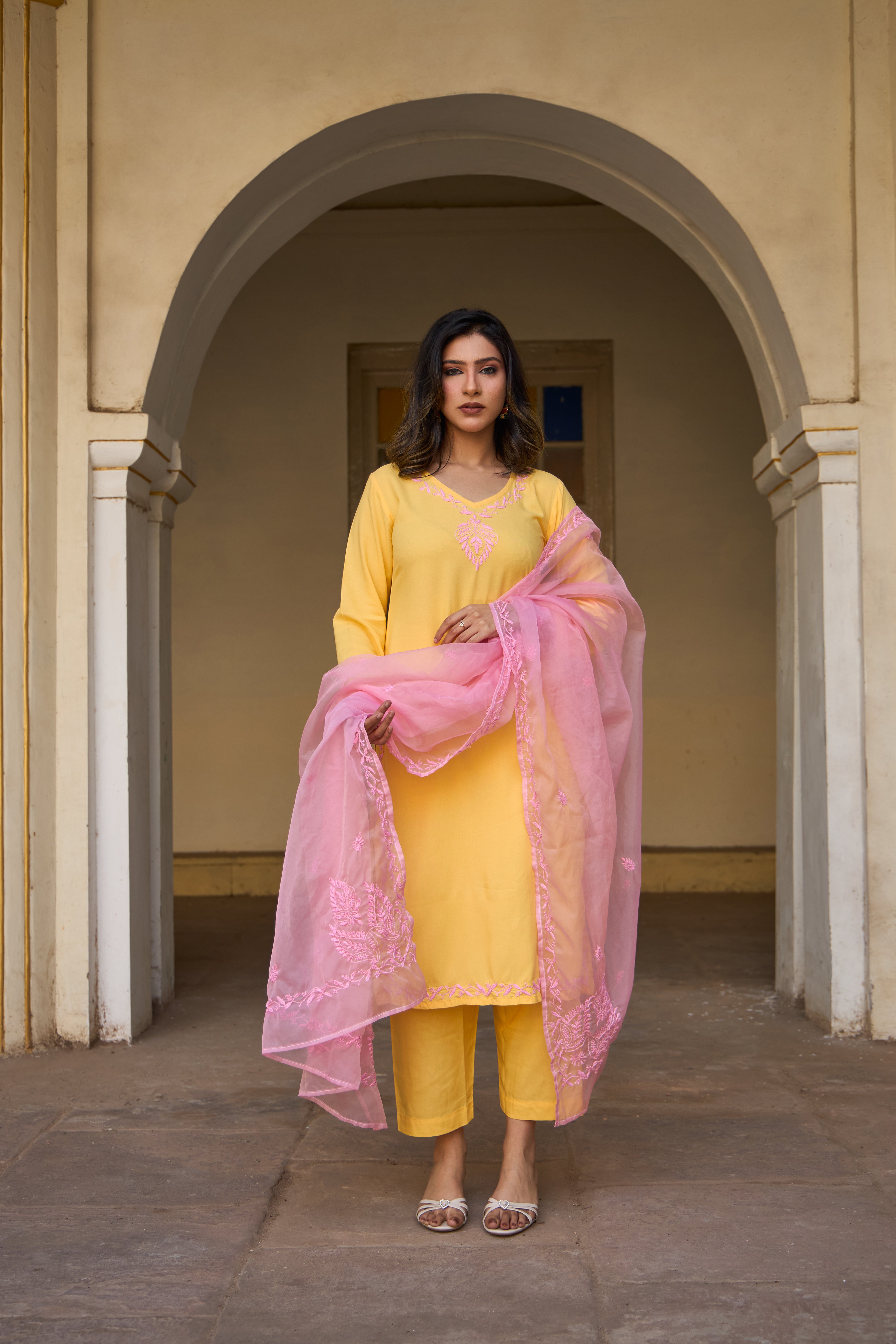 Woman in a yellow outfit with a pink embroidered organza dupatta standing in an archway.