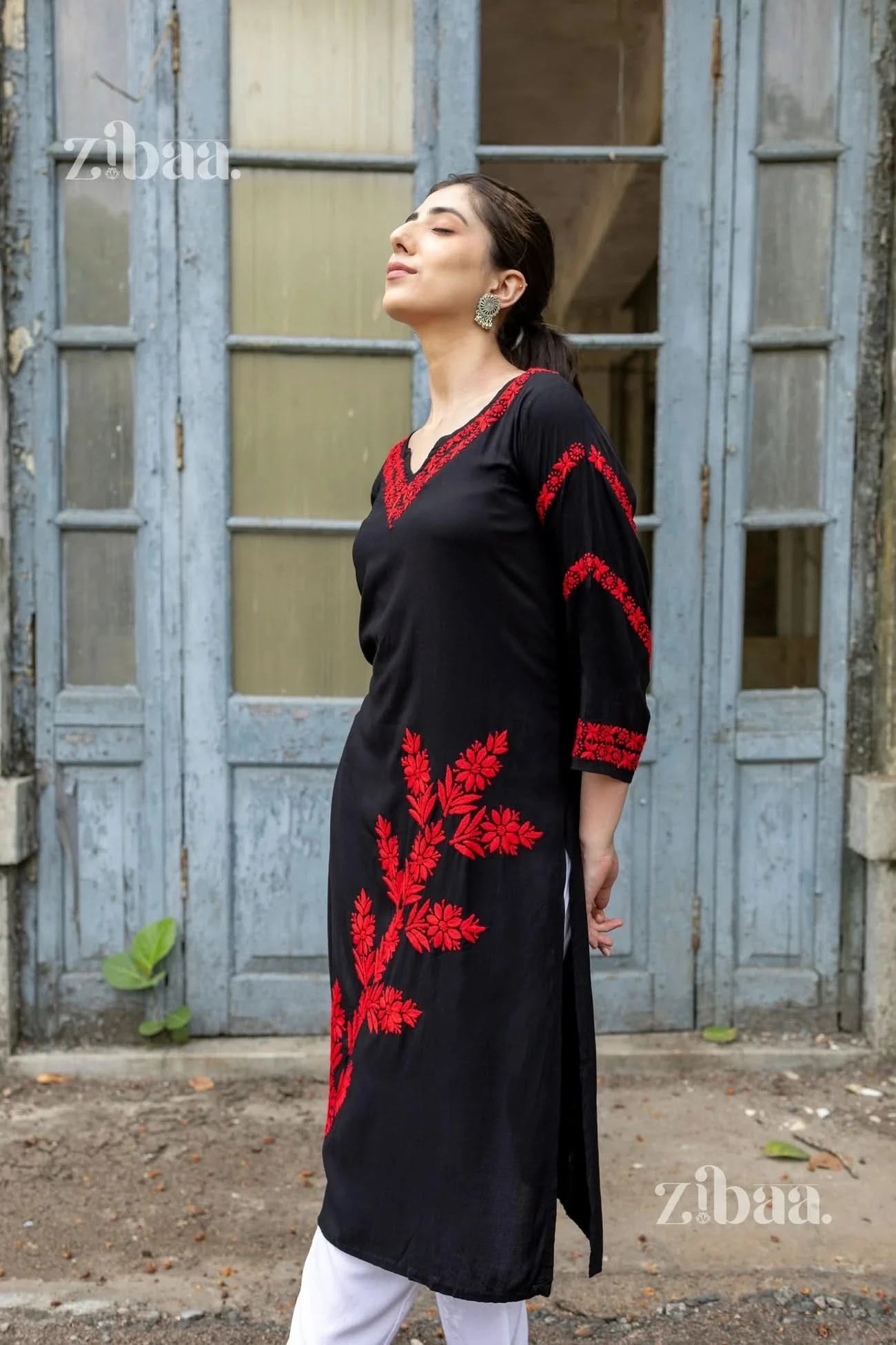 Woman wearing a black dress with red embroidery in front of a blue door.