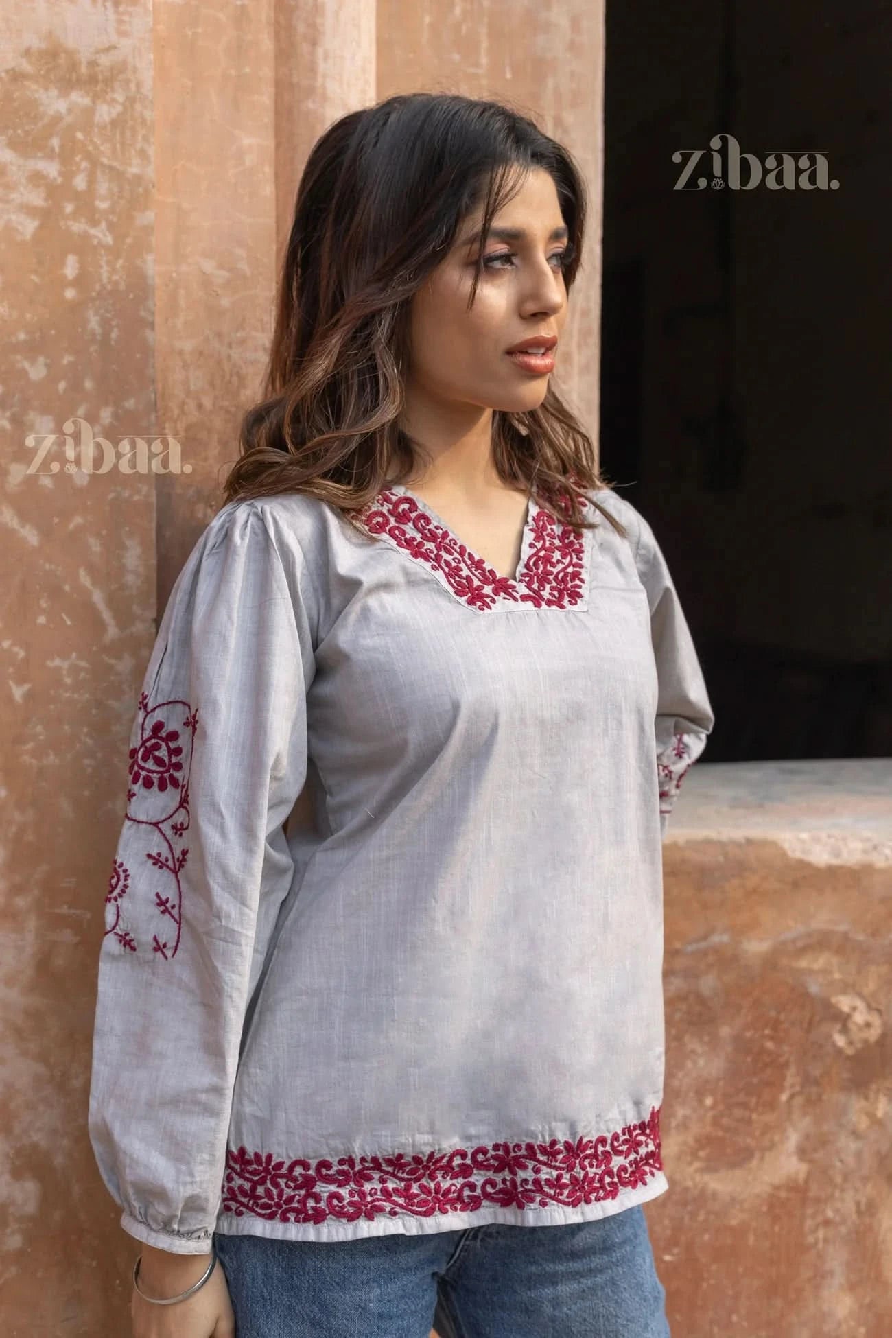 Woman standing outdoors in a stylish grey Chikankari top with intricate red embroidery on the neckline, sleeves, and hem, paired with jeans