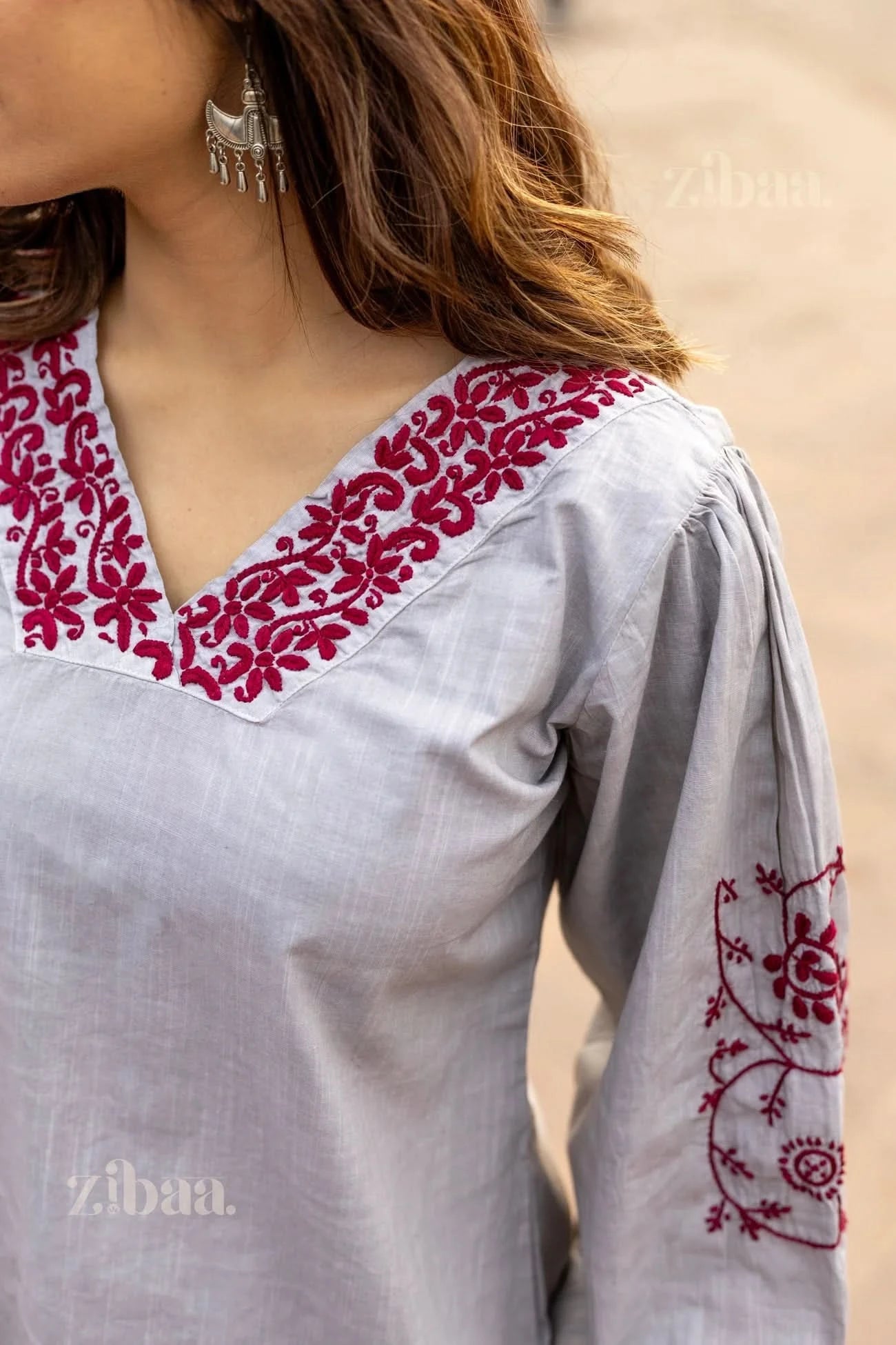 Partial view of a woman wearing a grey Chikankari top with red embroidery on the neckline and sleeves, paired with statement earrings