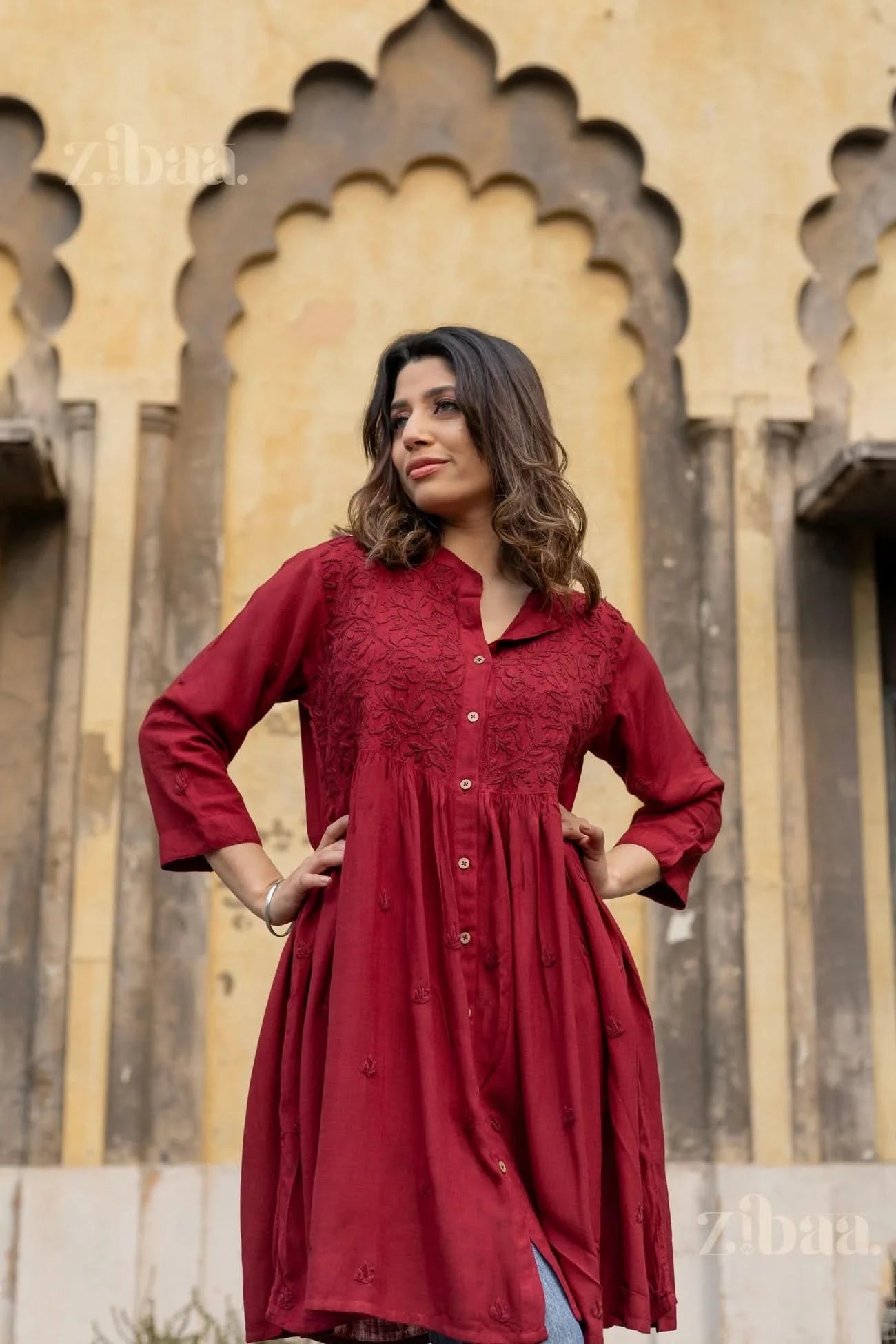 A woman poses with her hands on her hips, wearing a maroon Chikankari top, showcasing its intricate embroidery and flowy design.