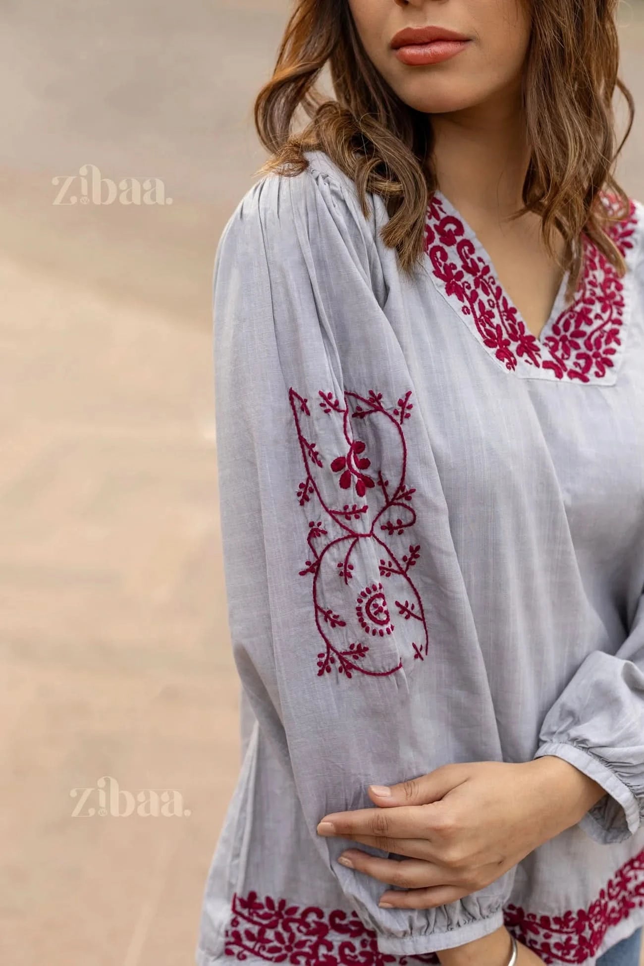 Close-up of a woman posing in a grey Chikankari top, featuring elegant red embroidery on the sleeves, neckline, and hemline