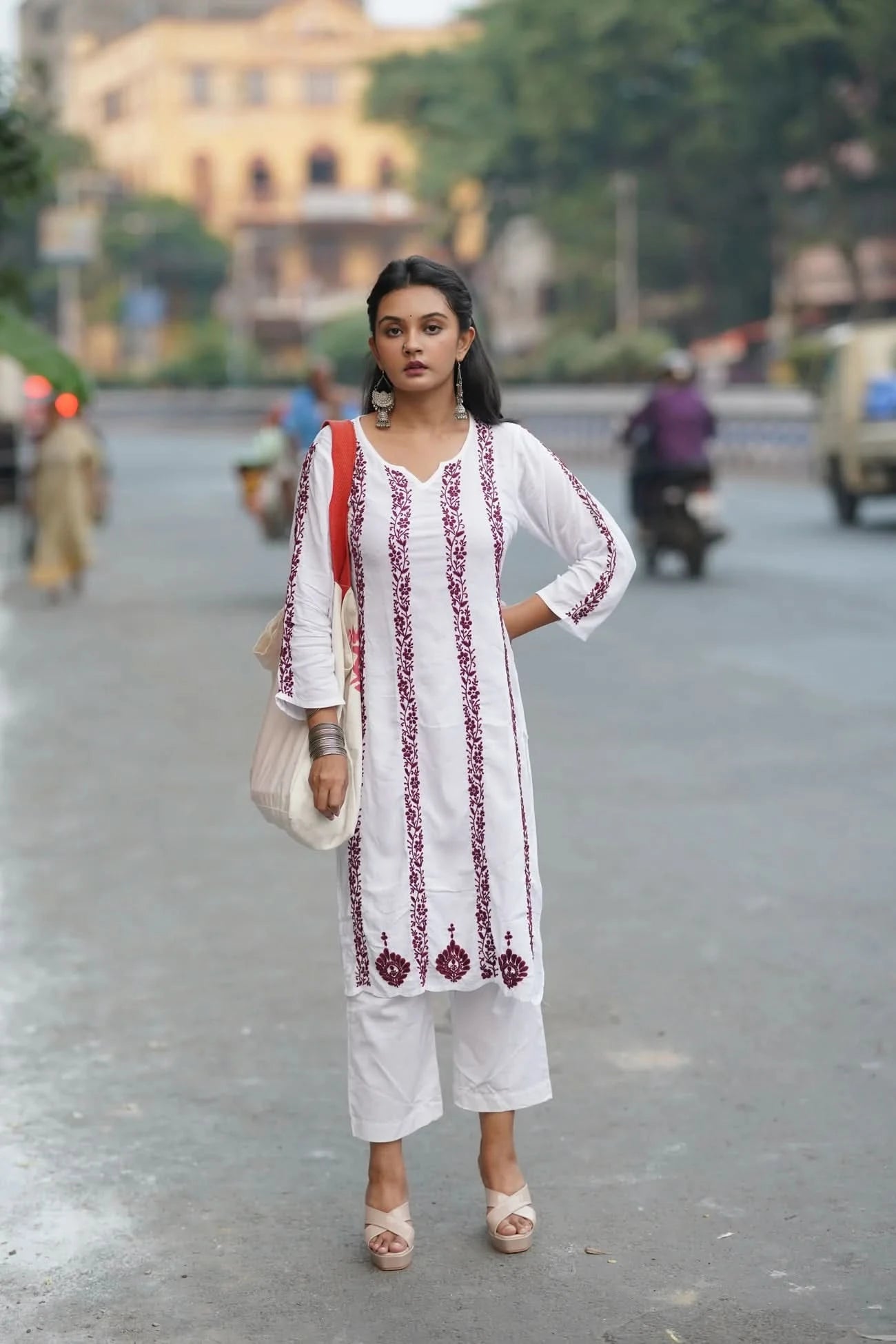 Woman in a white and red traditional outfit standing on a street.