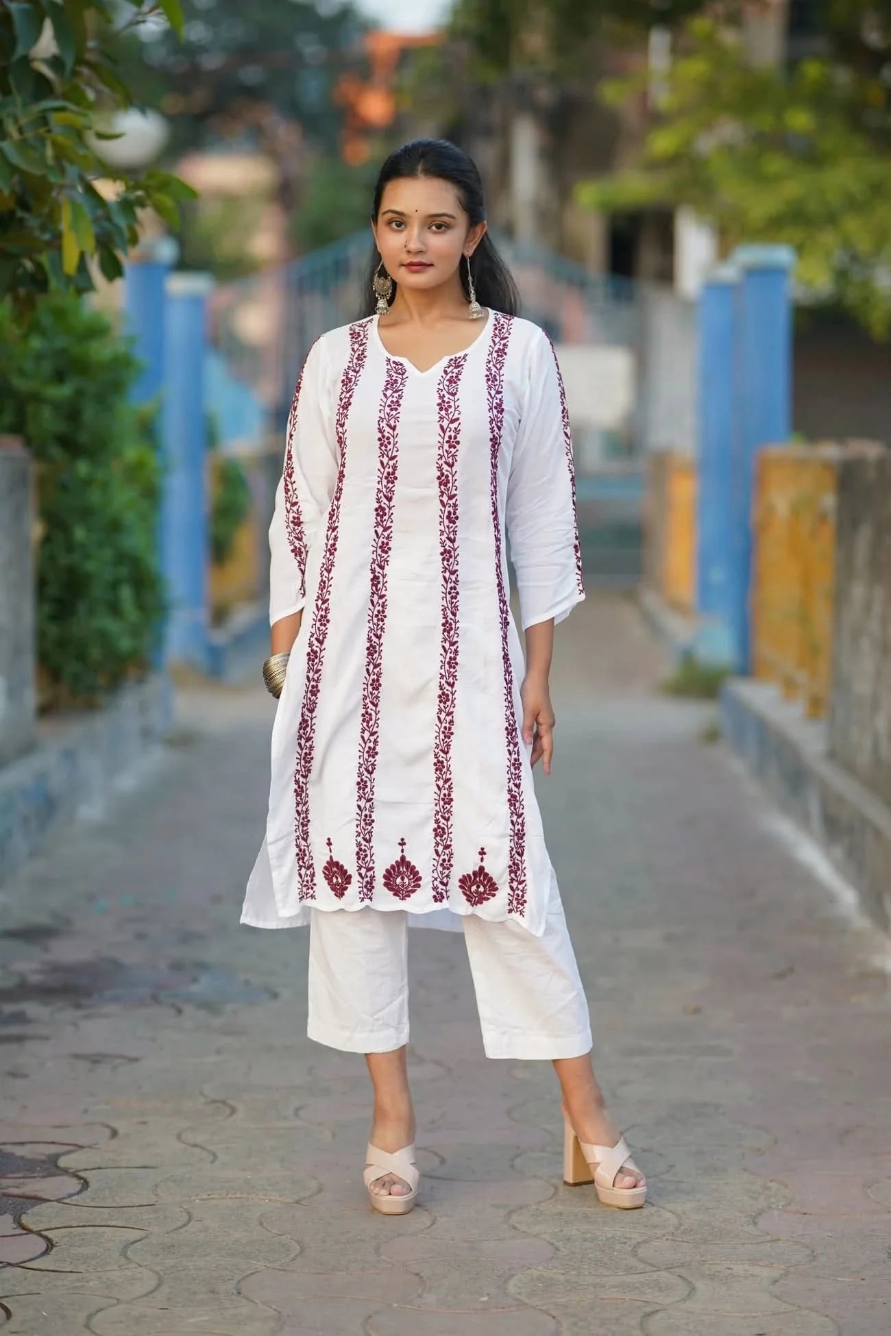 Woman wearing a white embroidered kurta with red patterns on a street.