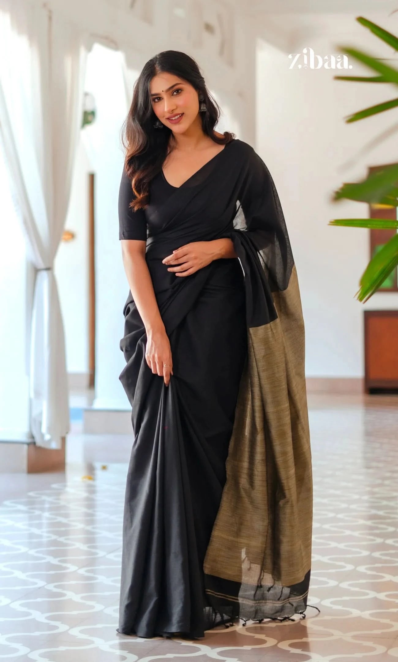 Woman in a black saree with a green border standing indoors.