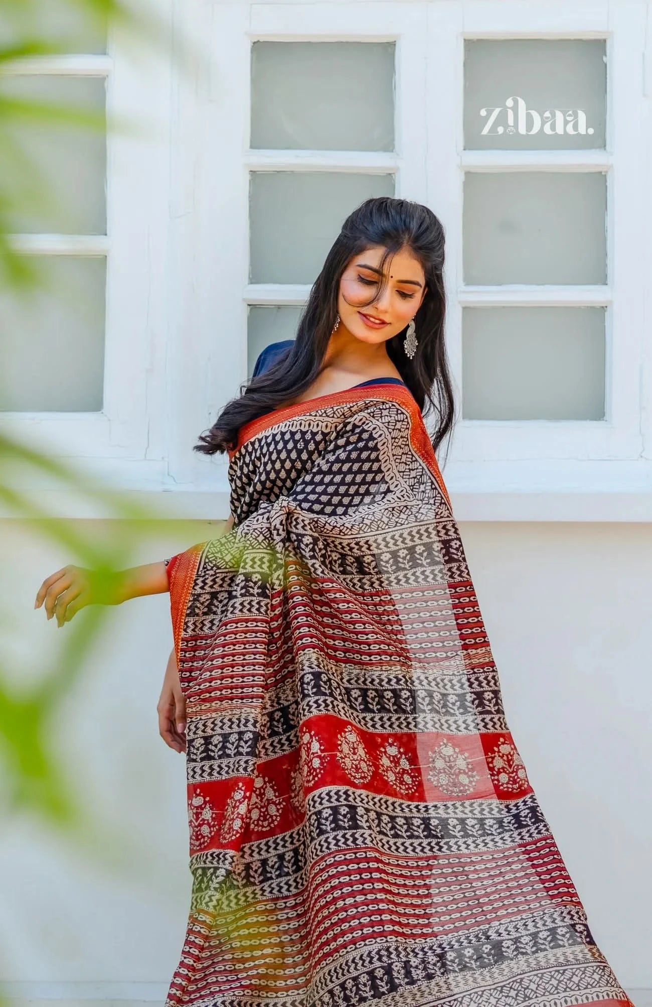 Woman wearing a patterned saree with a blurred background and 'zibaa' branding.