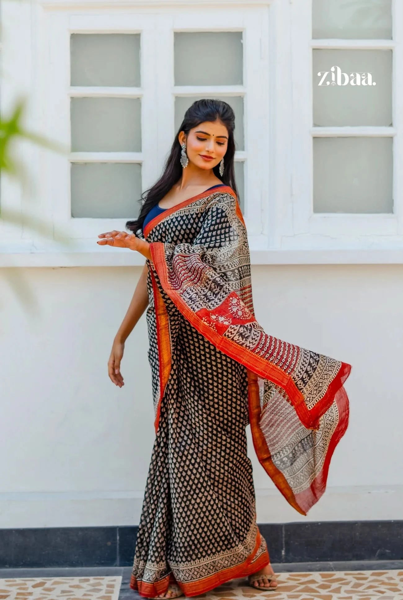 Woman wearing a patterned saree with a white window and 'Zibba' branding in the background