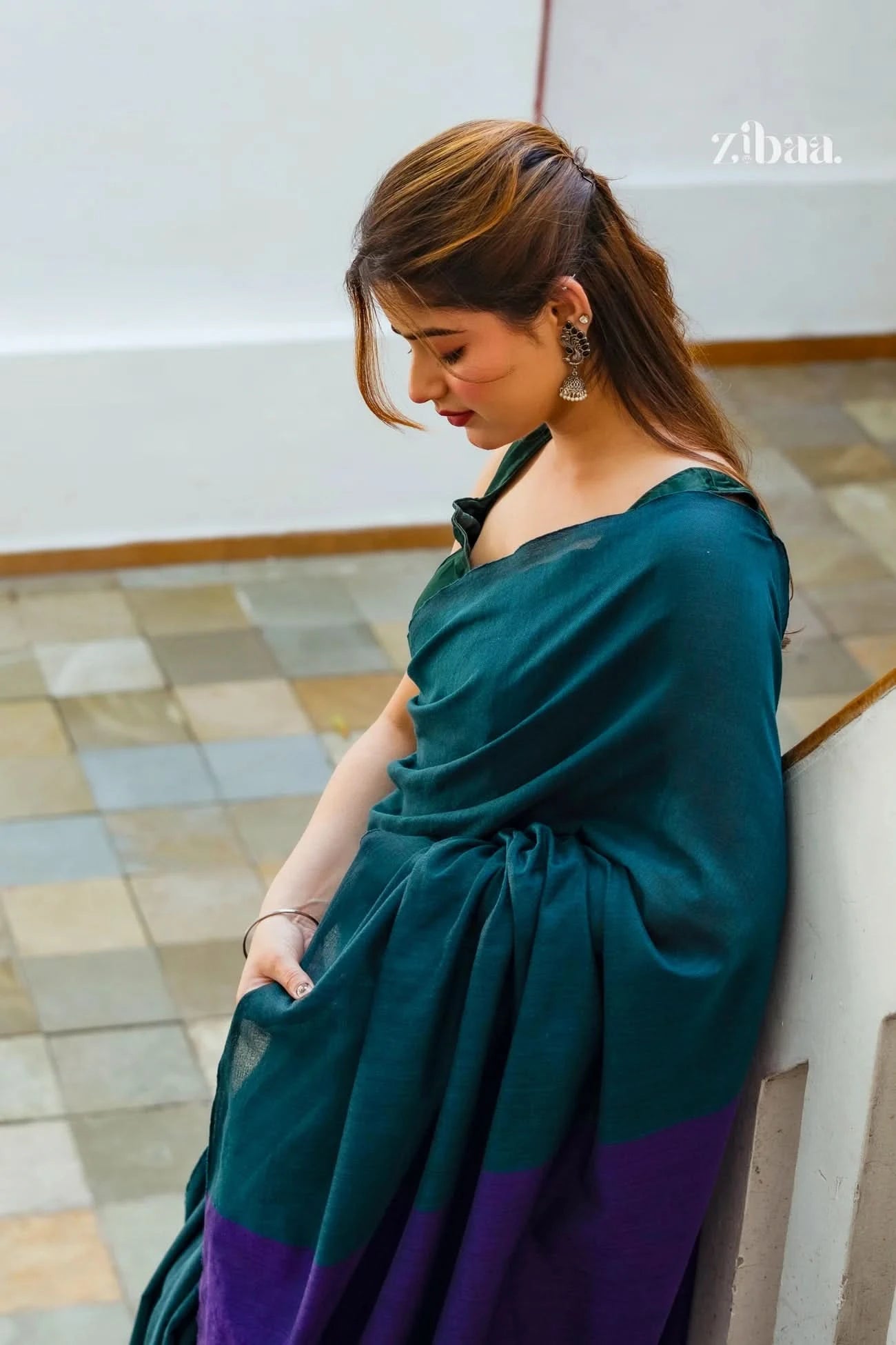 Woman wearing a green and purple dress leaning against a wall.