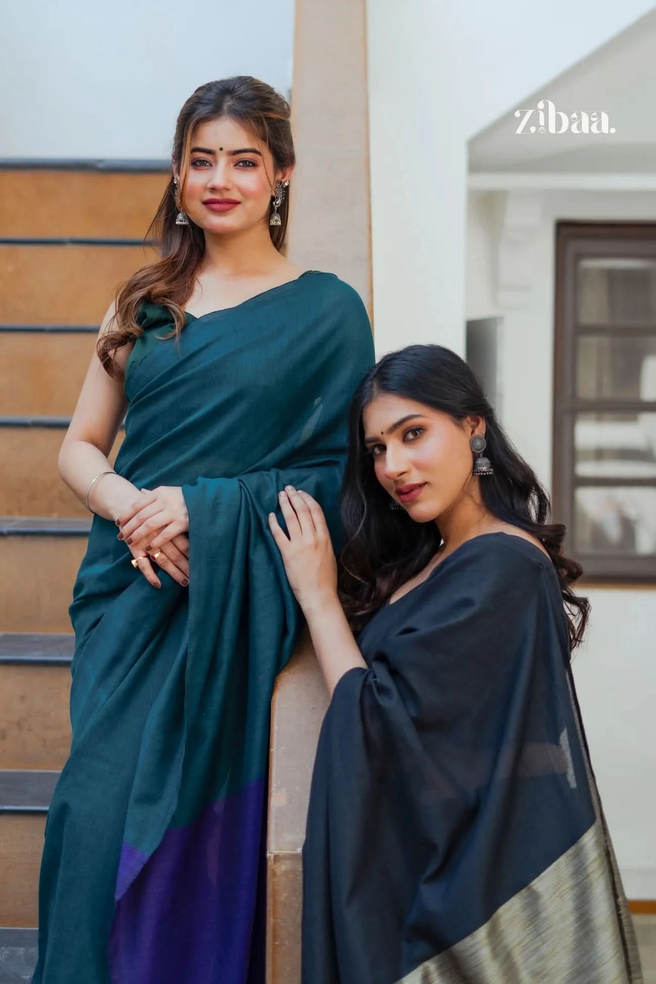 Two women in sarees standing outdoors with a building in the background