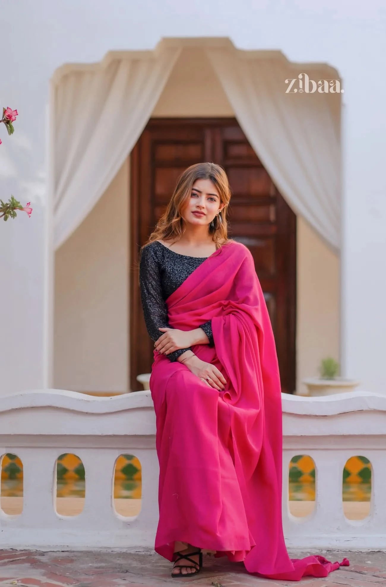 Woman in a pink saree standing in front of a decorative archway.
