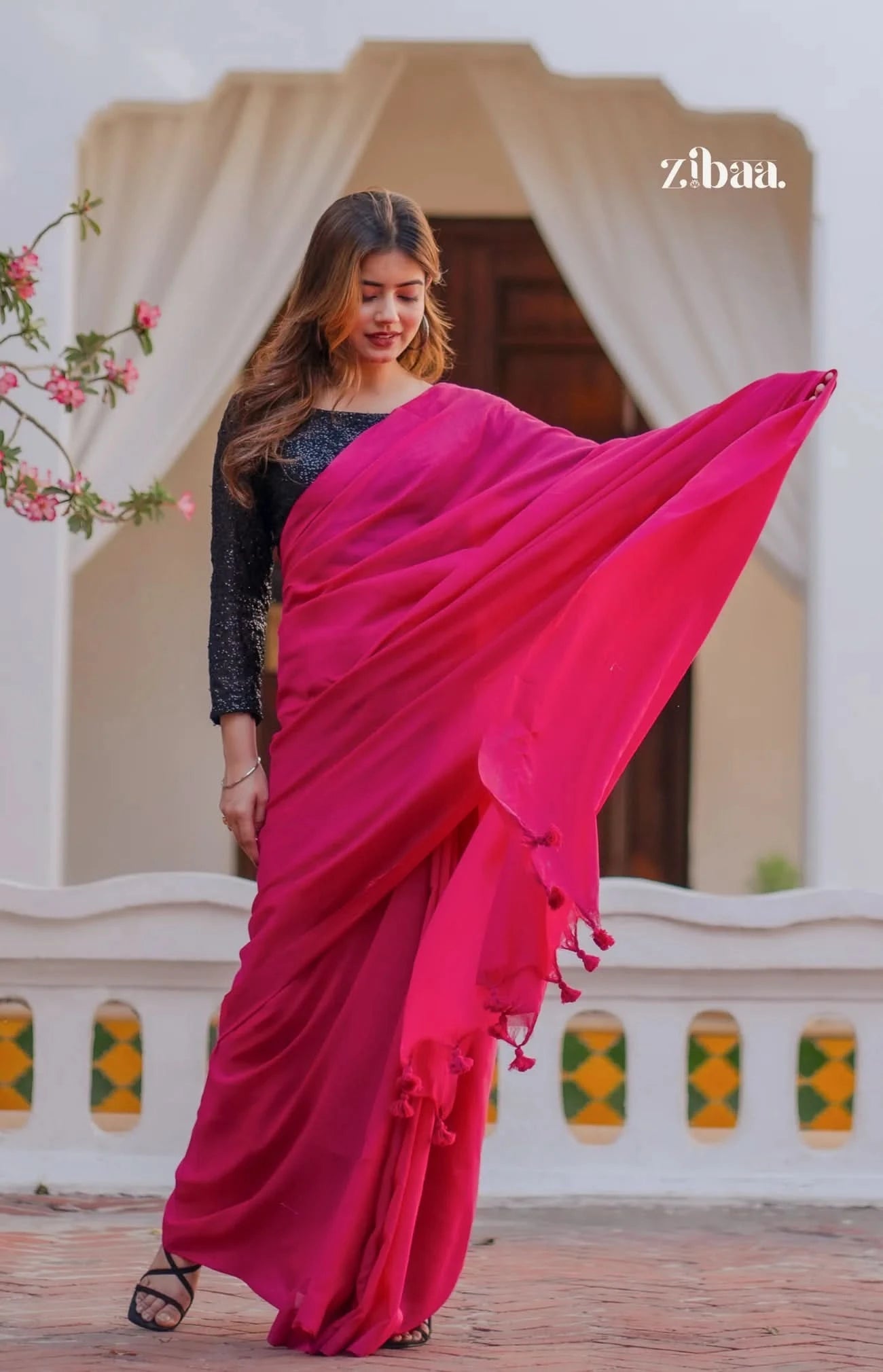 Woman wearing a bright pink saree with a blurred decorative background