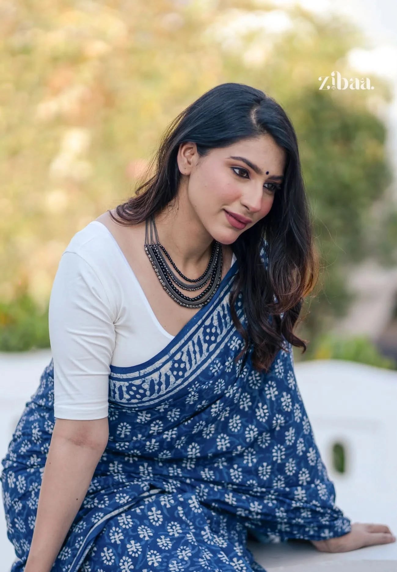 Woman wearing a blue saree with white patterns sitting outdoors.