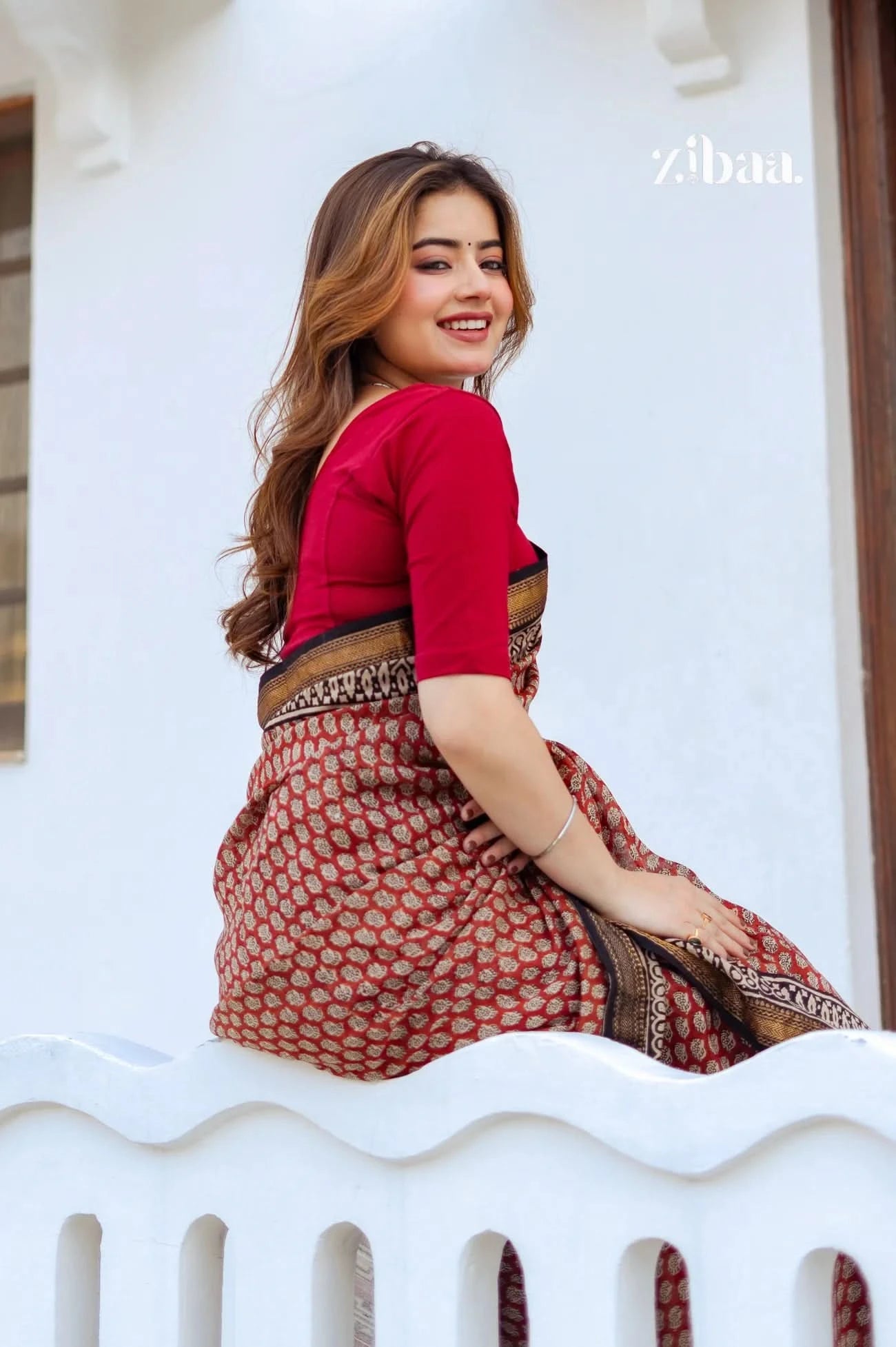 Woman in a red and brown traditional outfit sitting on a white railing.