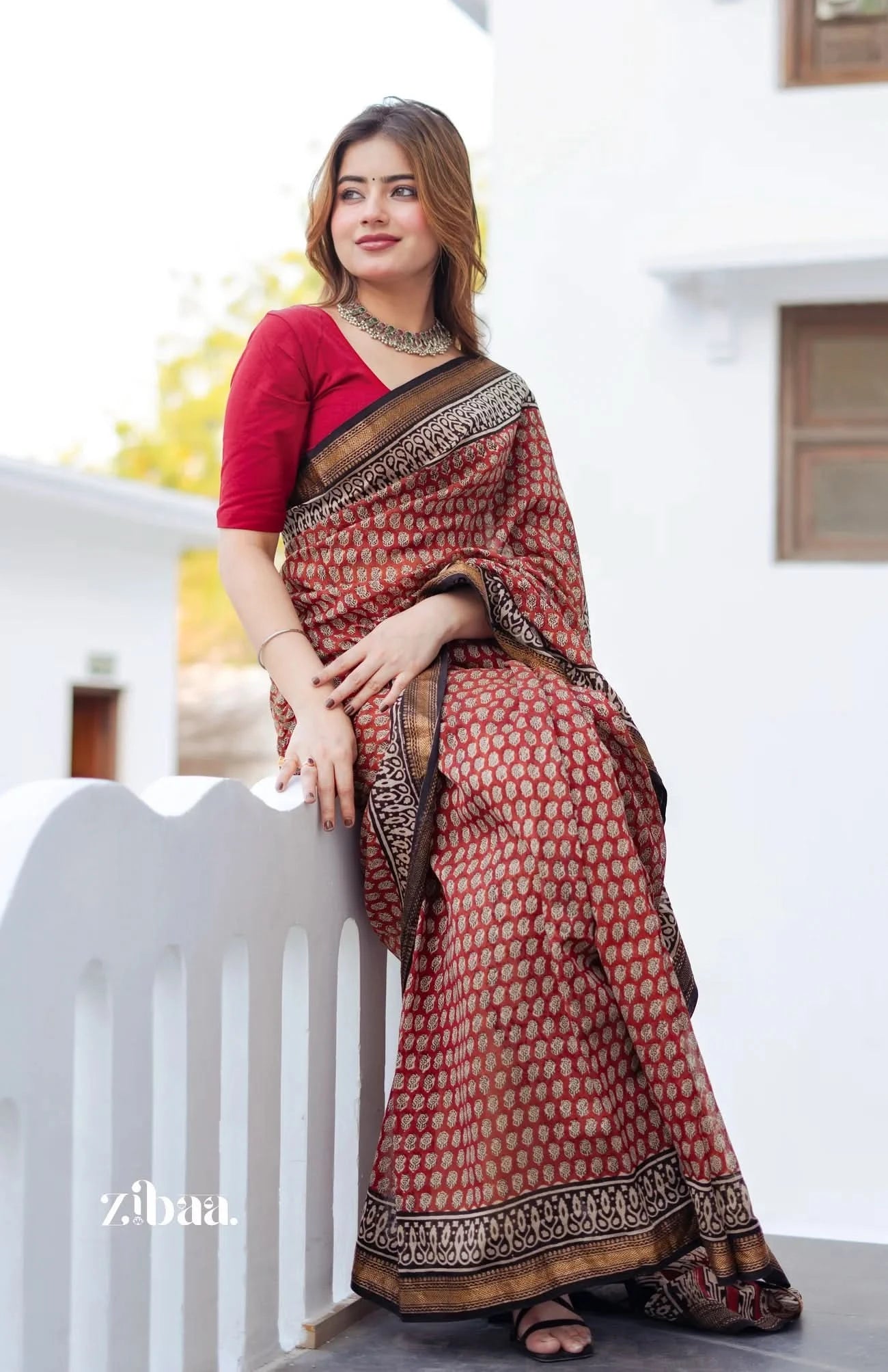 Woman wearing a patterned saree sitting on a white railing.