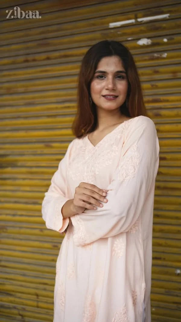 Woman in a light pink saree standing in front of a yellow shutter.