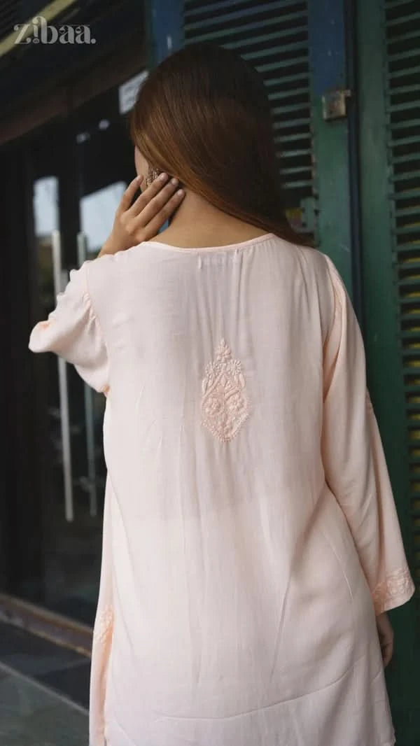 Woman wearing a light pink embroidered dress standing in front of a building entrance.