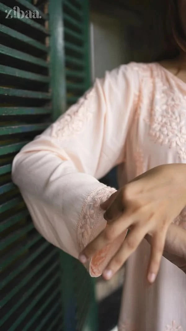 Close-up of a person wearing a light pink lace-trimmed dress with green vertical blinds in the background.