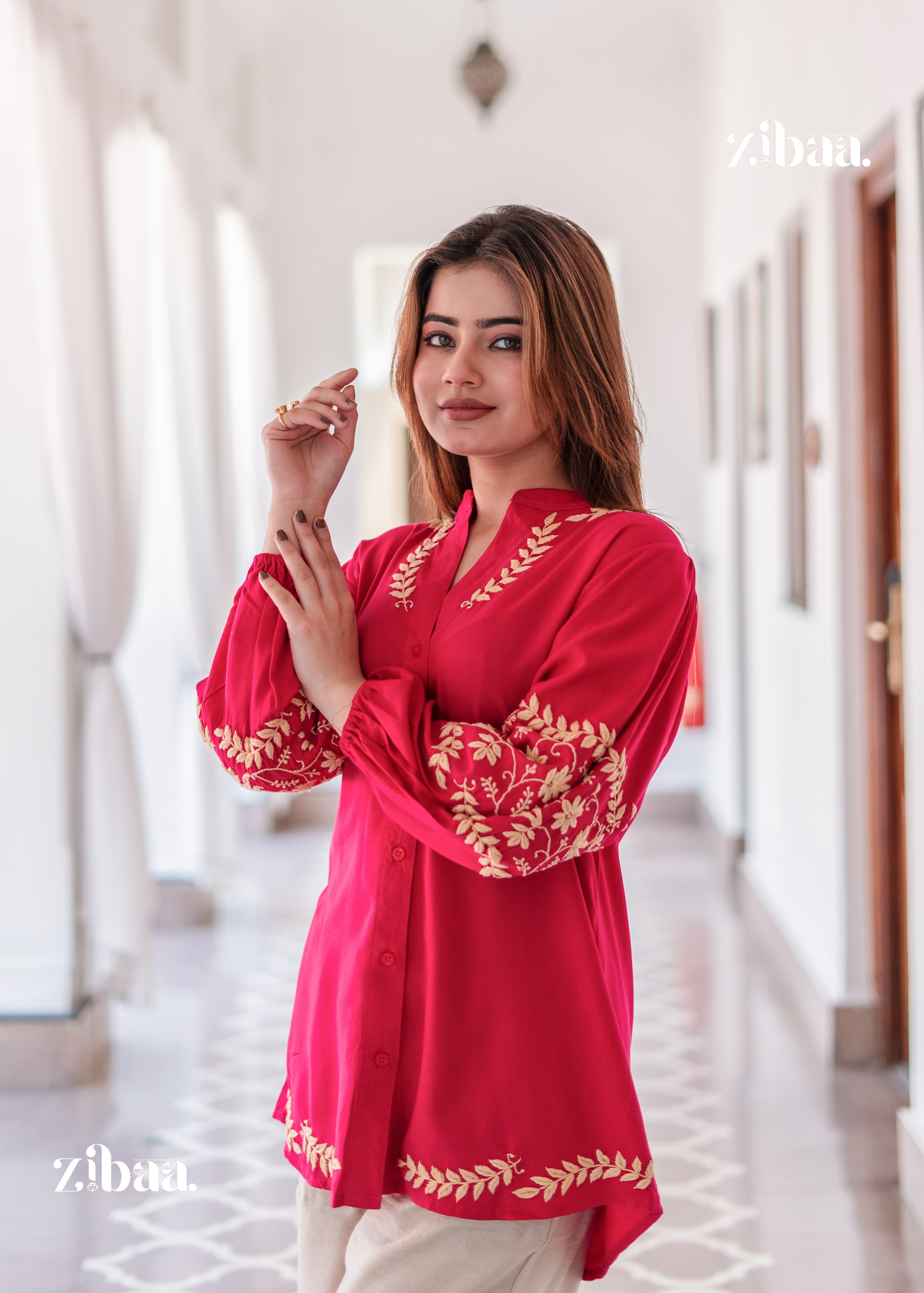 The model poses softly by a white curtain in a Festive Hot Pink Kurta with Intricate Detailing. Festive Hot Pink Kurta with Intricate Detailing is styled with beige bottoms for a subtle contrast. The golden embroidery enhances the festive charm of the outfit.