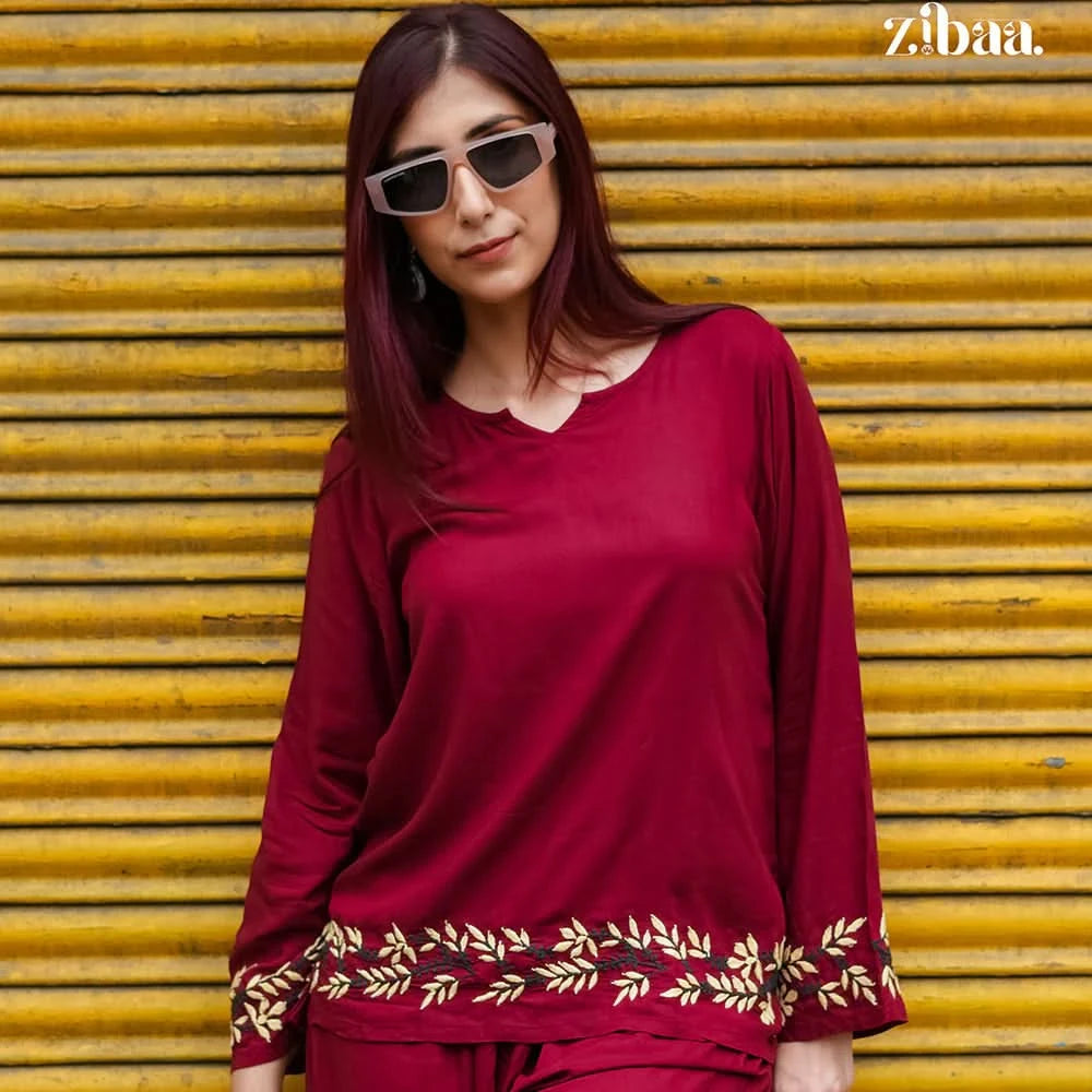 Woman wearing a red outfit with gold embroidery in front of a yellow shutter, branded 'zibaa'.