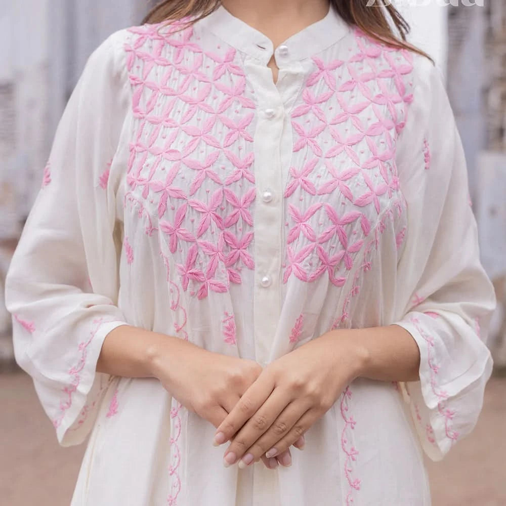 White shirt with pink floral embroidery worn by a person, blurred background