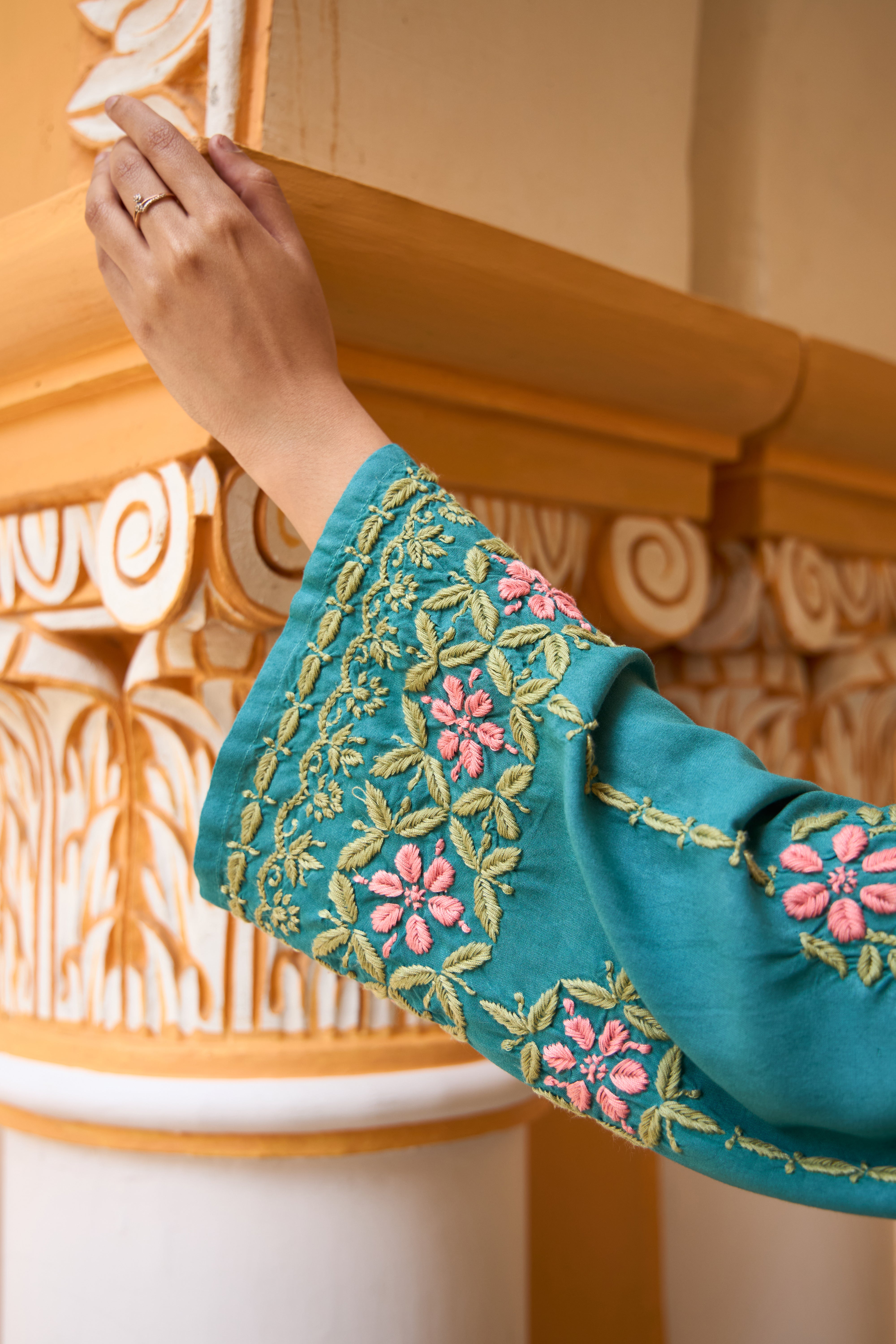 Close-up of a teal sleeve with floral embroidery against an ornate background