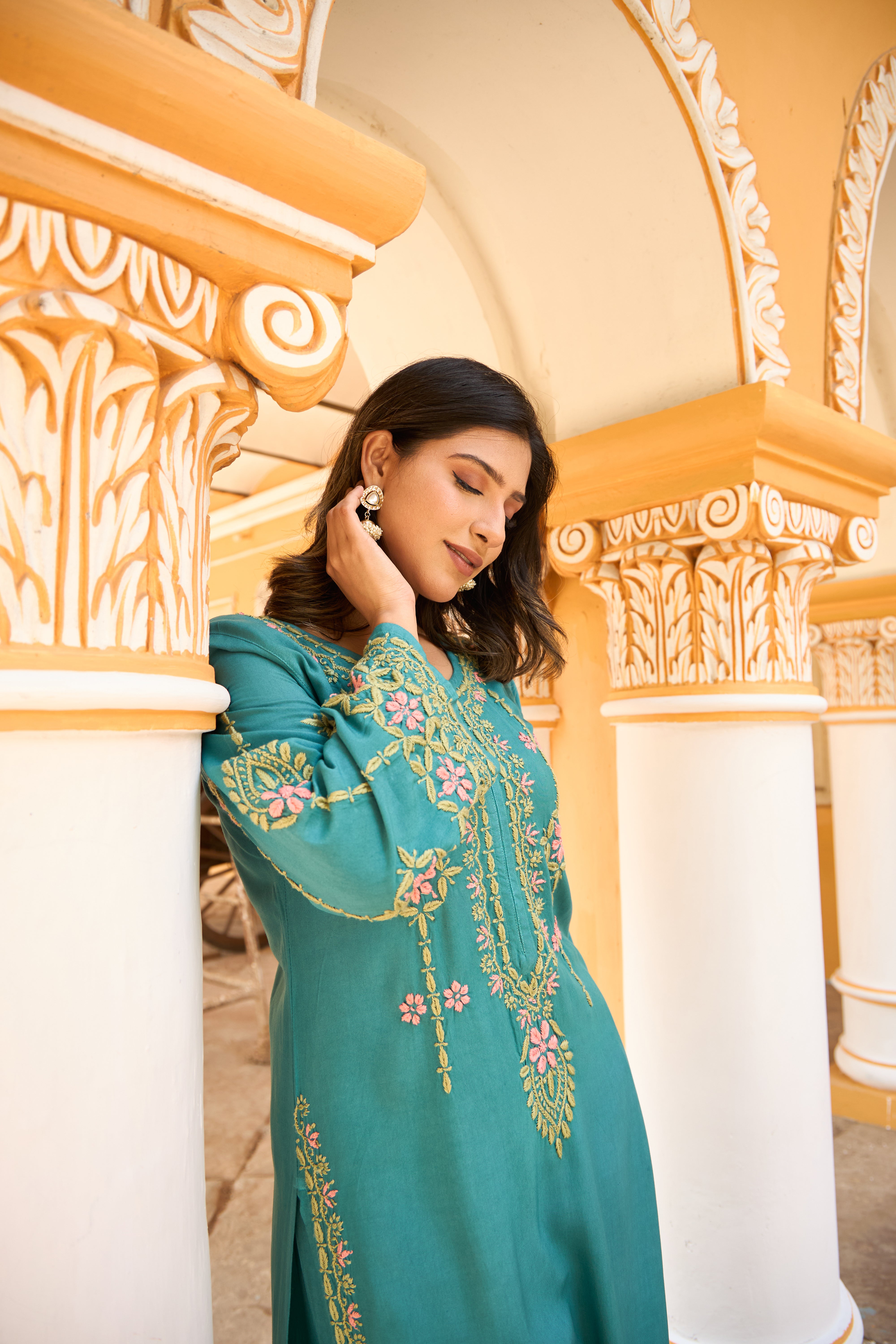 Woman in a teal Chikankari kurta set standing in an ornate architectural setting