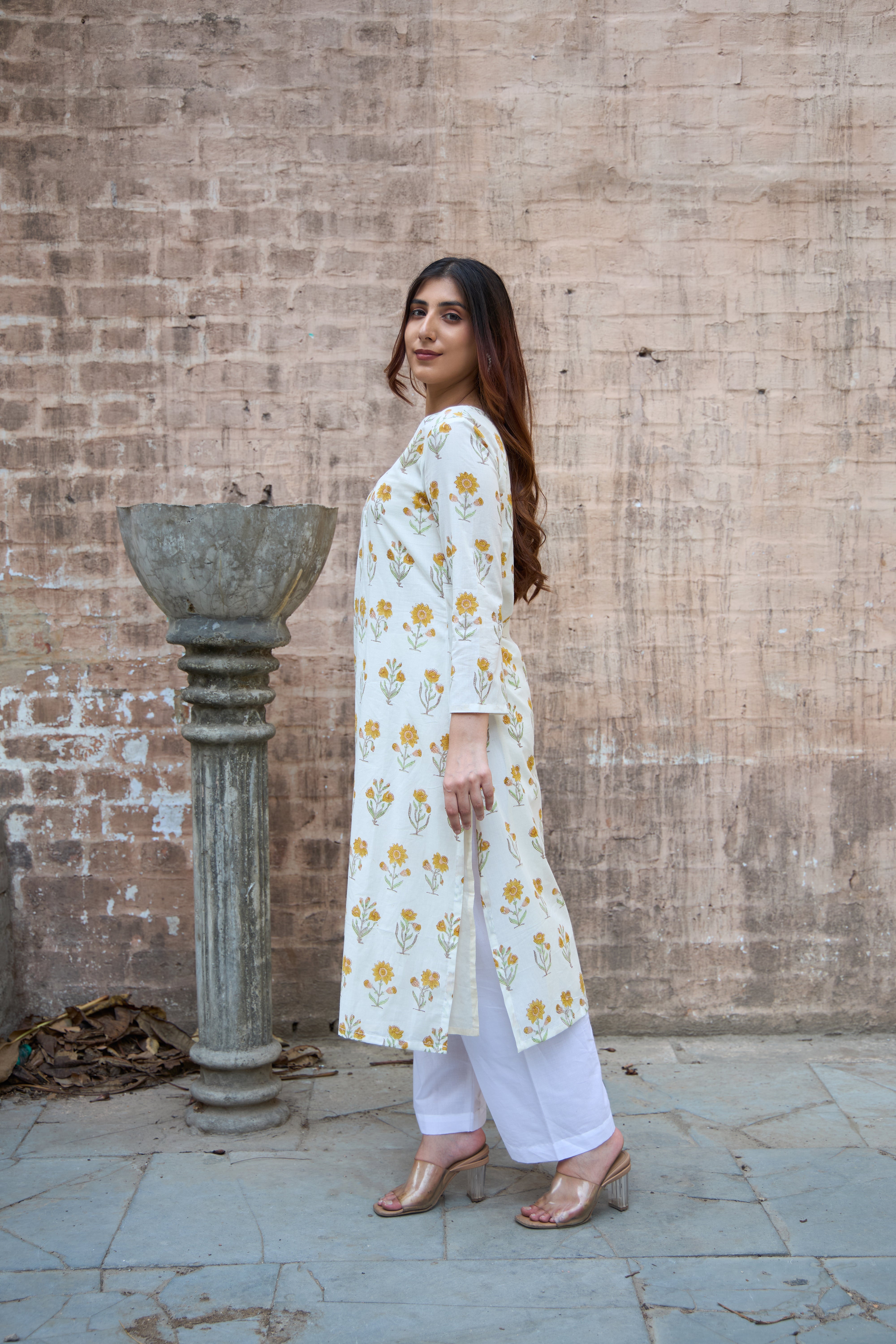 Woman in a white floral dress standing against a textured brick wall.