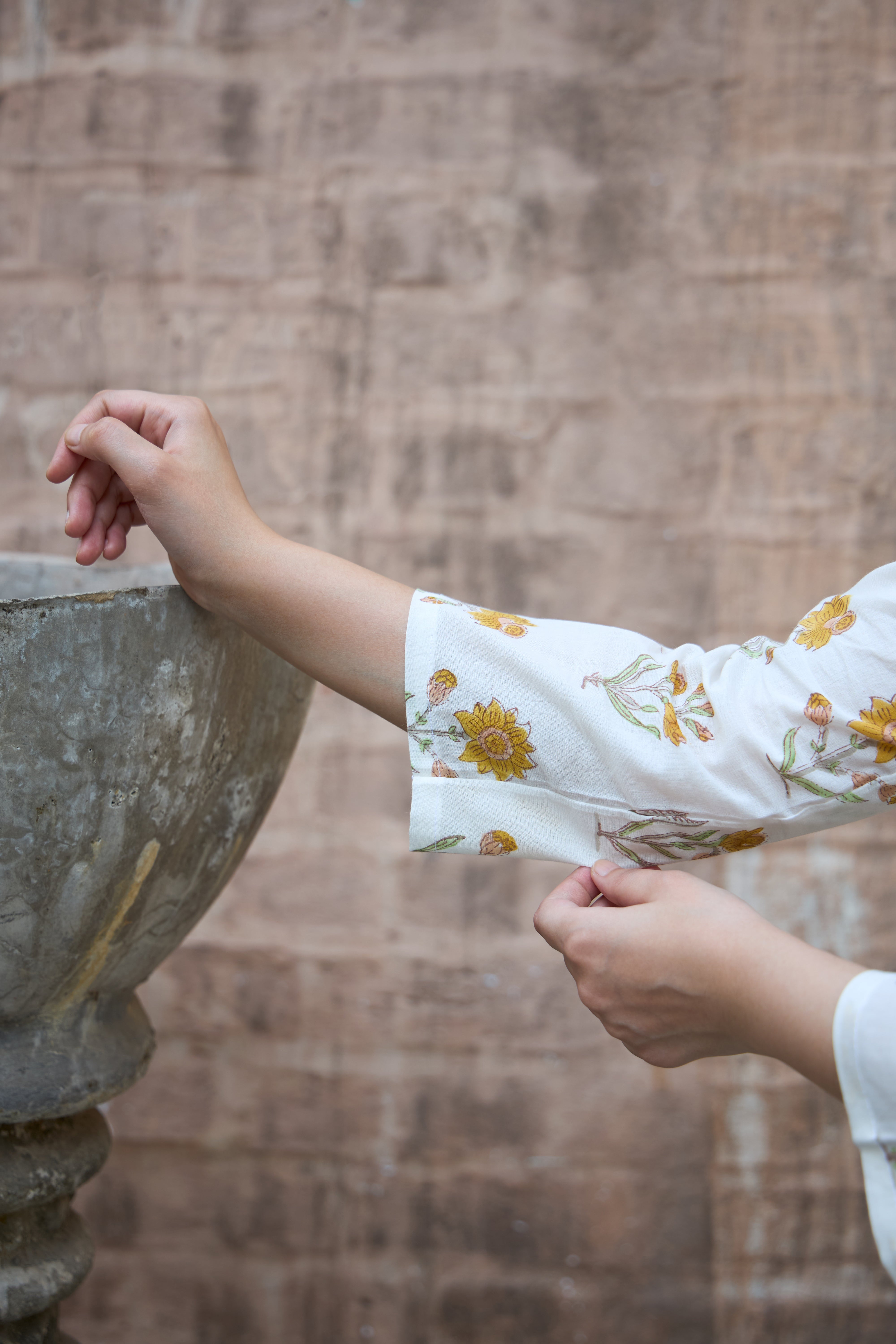 Person wearing a white sleeve with floral pattern against a stone wall.