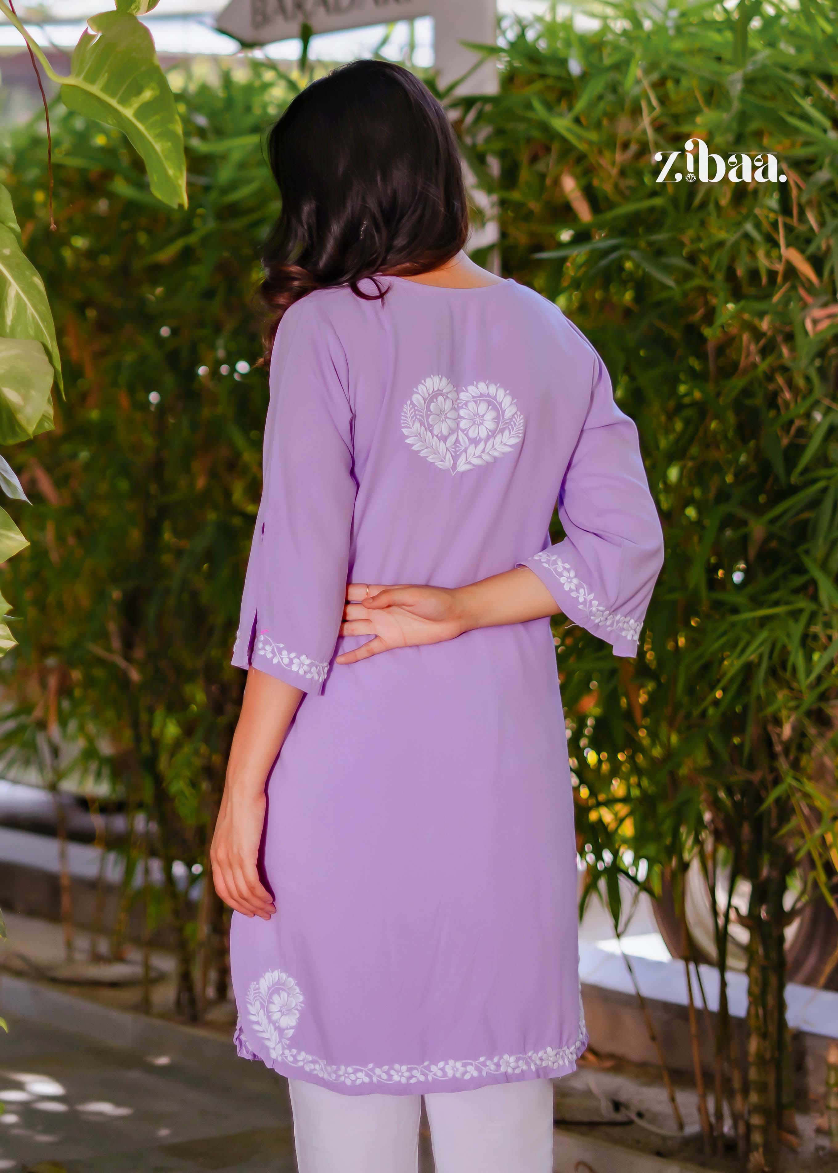 With her back turned, the model highlights the detailed chikankari embroidery on the back of her lavender chikankari kurti, set in an outdoor setting.