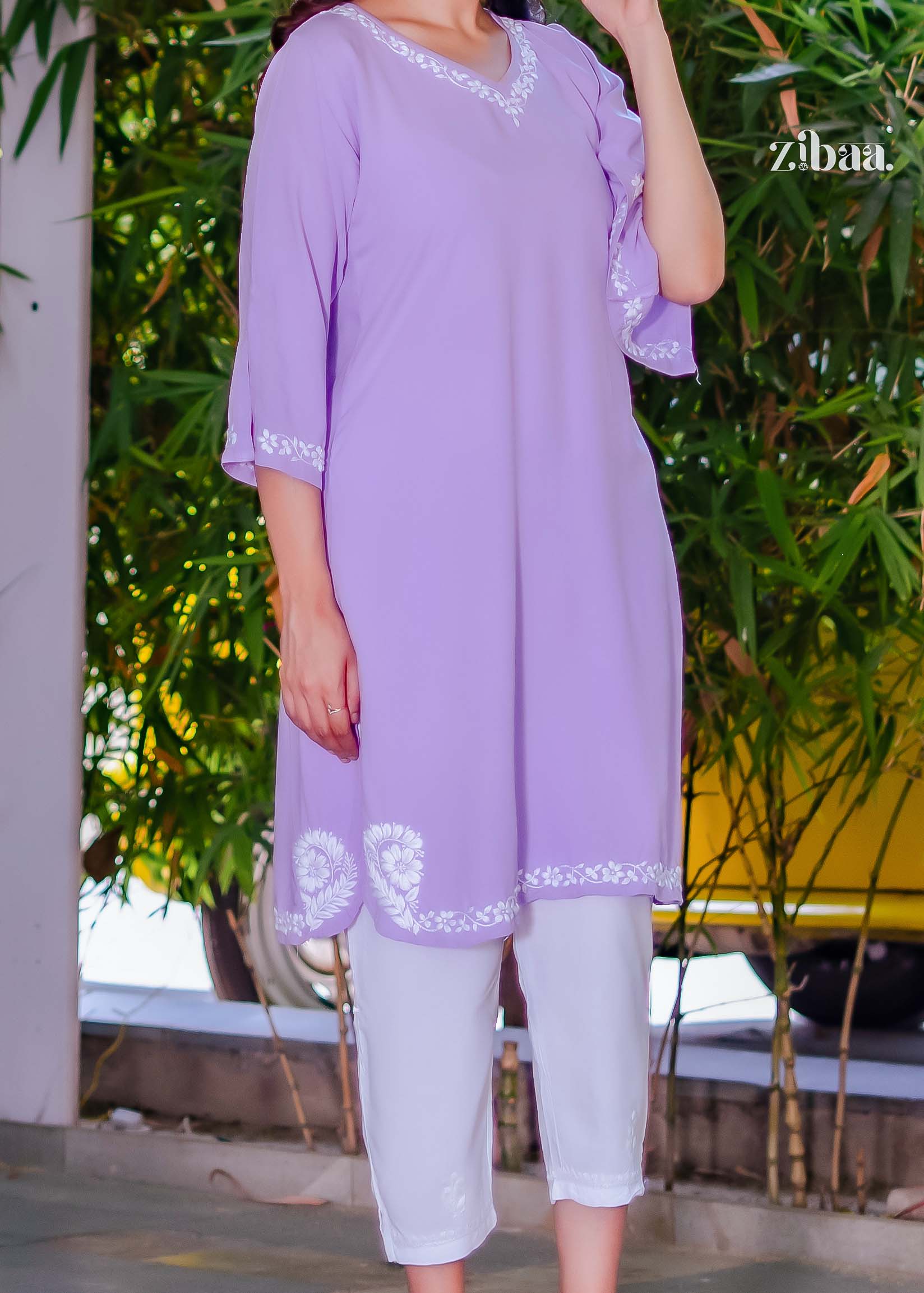 Model showing lavender chikankari kurta close-up with embroidered neckline. She folds her arm slightly, highlighting sleeve embroidery.
