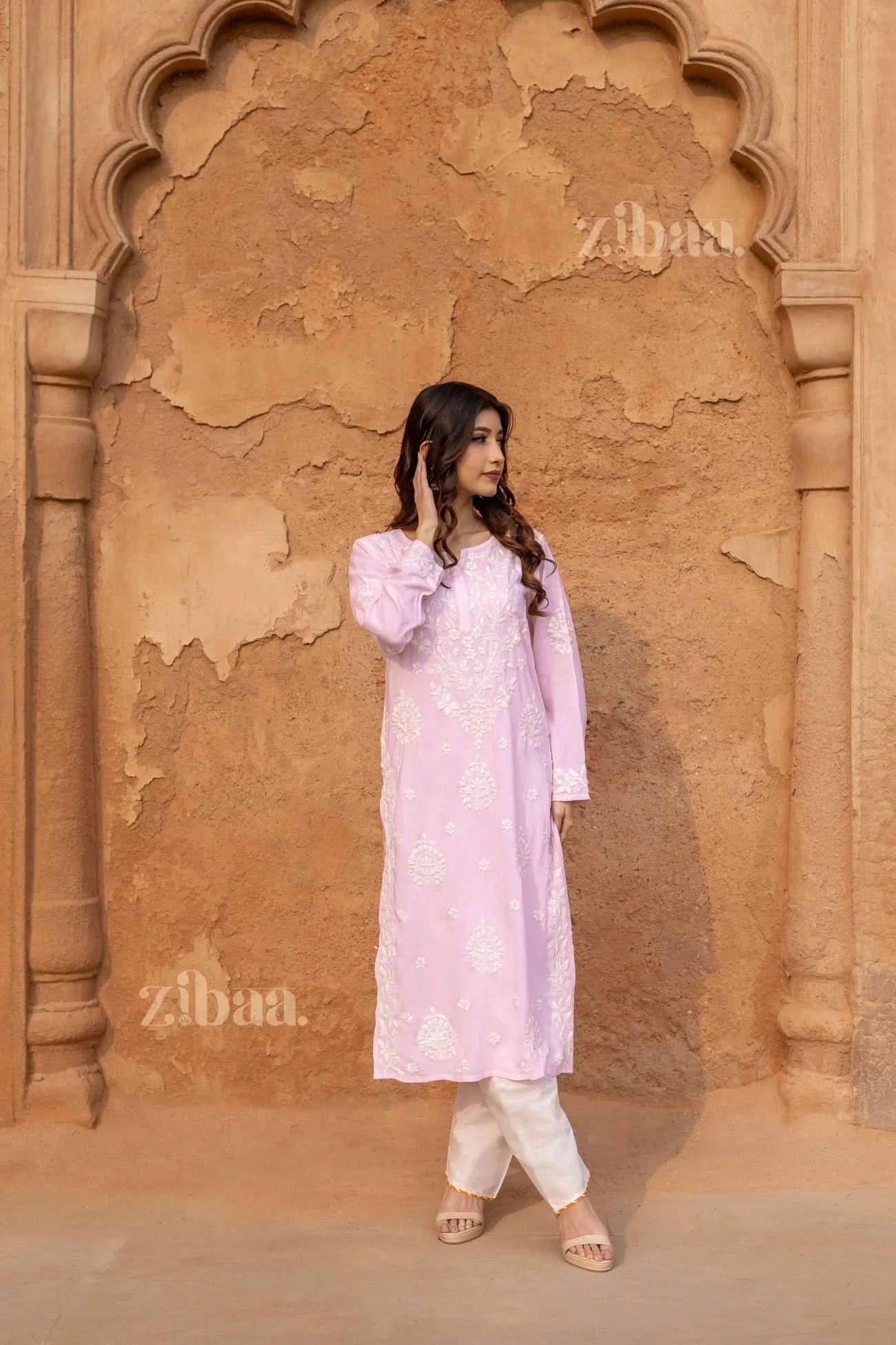 Model showcasing a pink Lucknowi Kurti with delicate white embroidery, standing confidently against a beautifully aged heritage wall.