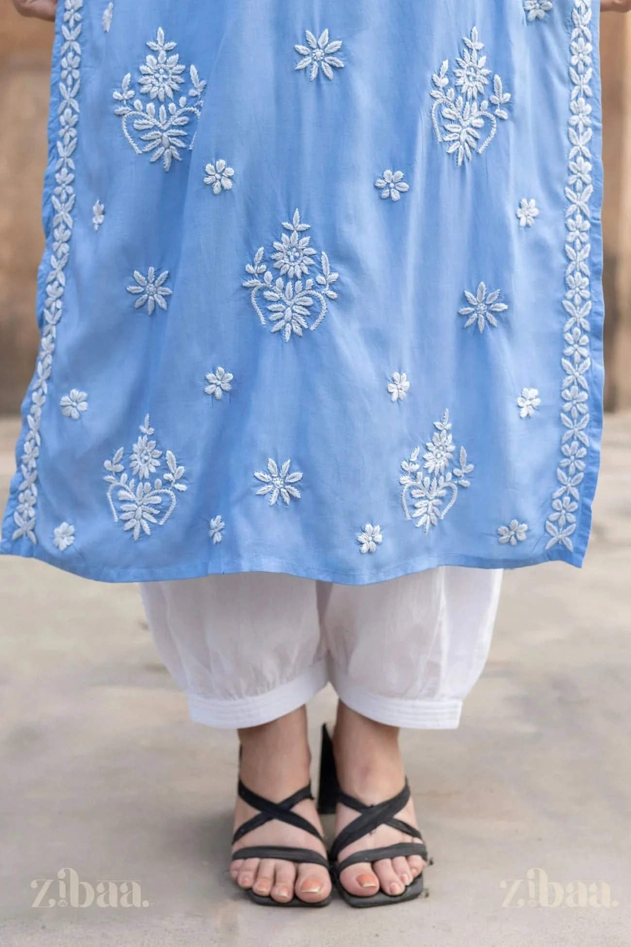 Close up shot of a Blue Lucknowi Kurta with intricate fine white embroidery styling with white pants along with black strappy sandals.