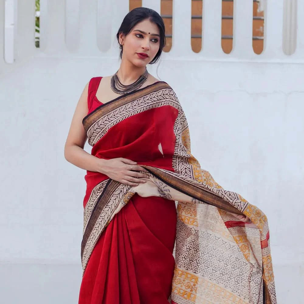 Woman wearing a red saree with a patterned border against a white background