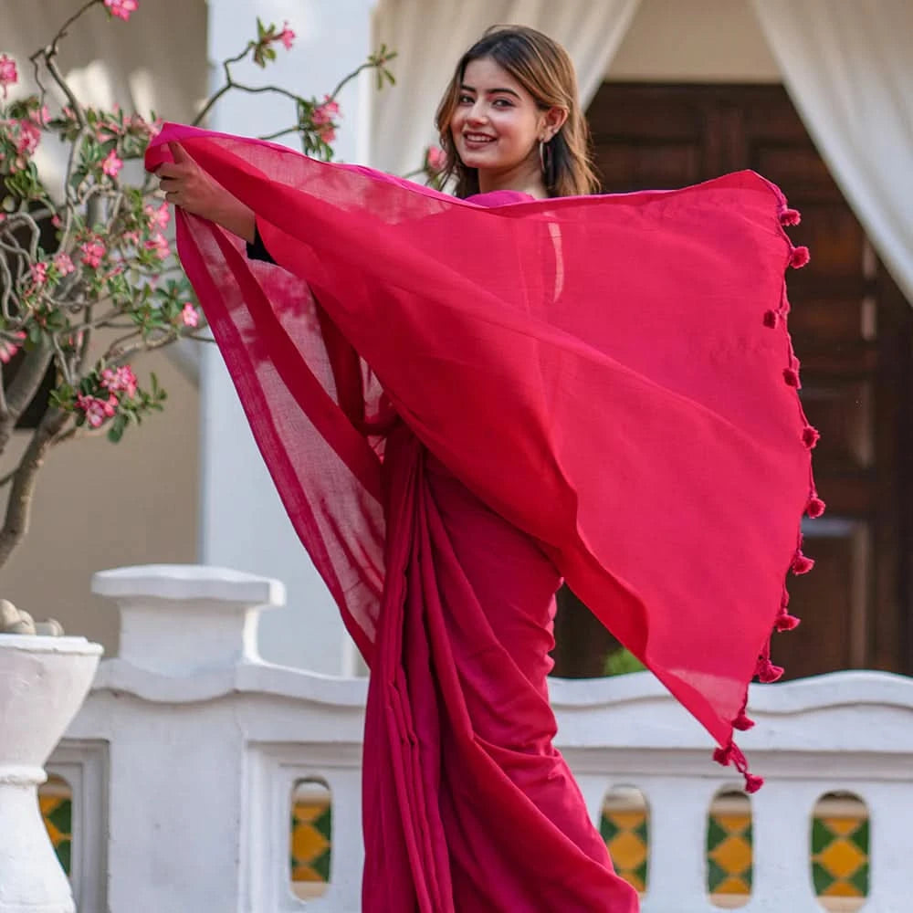 Woman in a bright pink saree with floral decorations, standing outdoors.