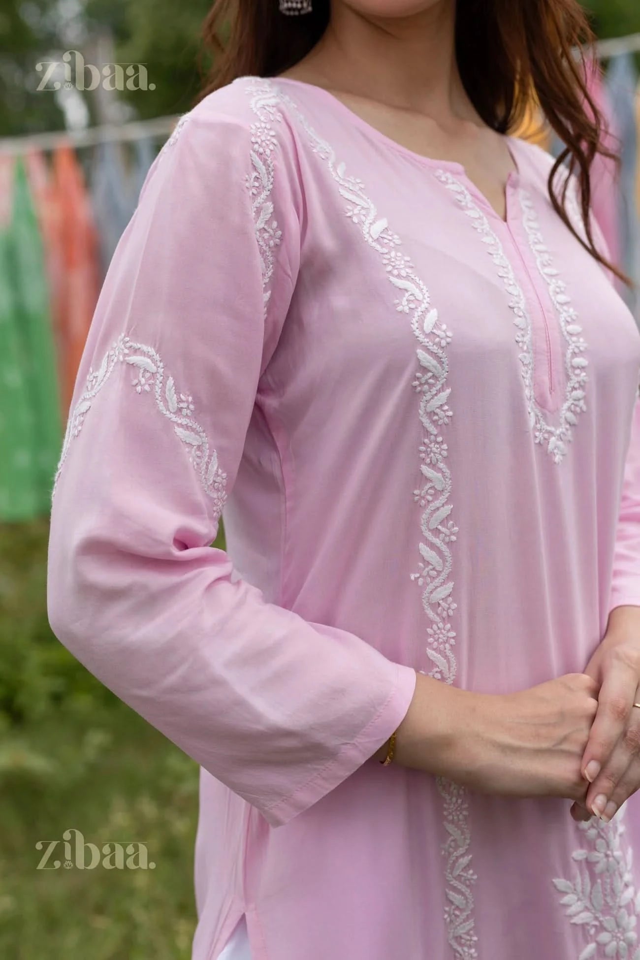 Close-up in detail of the Pink Chikankari kurti with heavy white embroidery on the neck and sleeves putting in an outdoor setting.